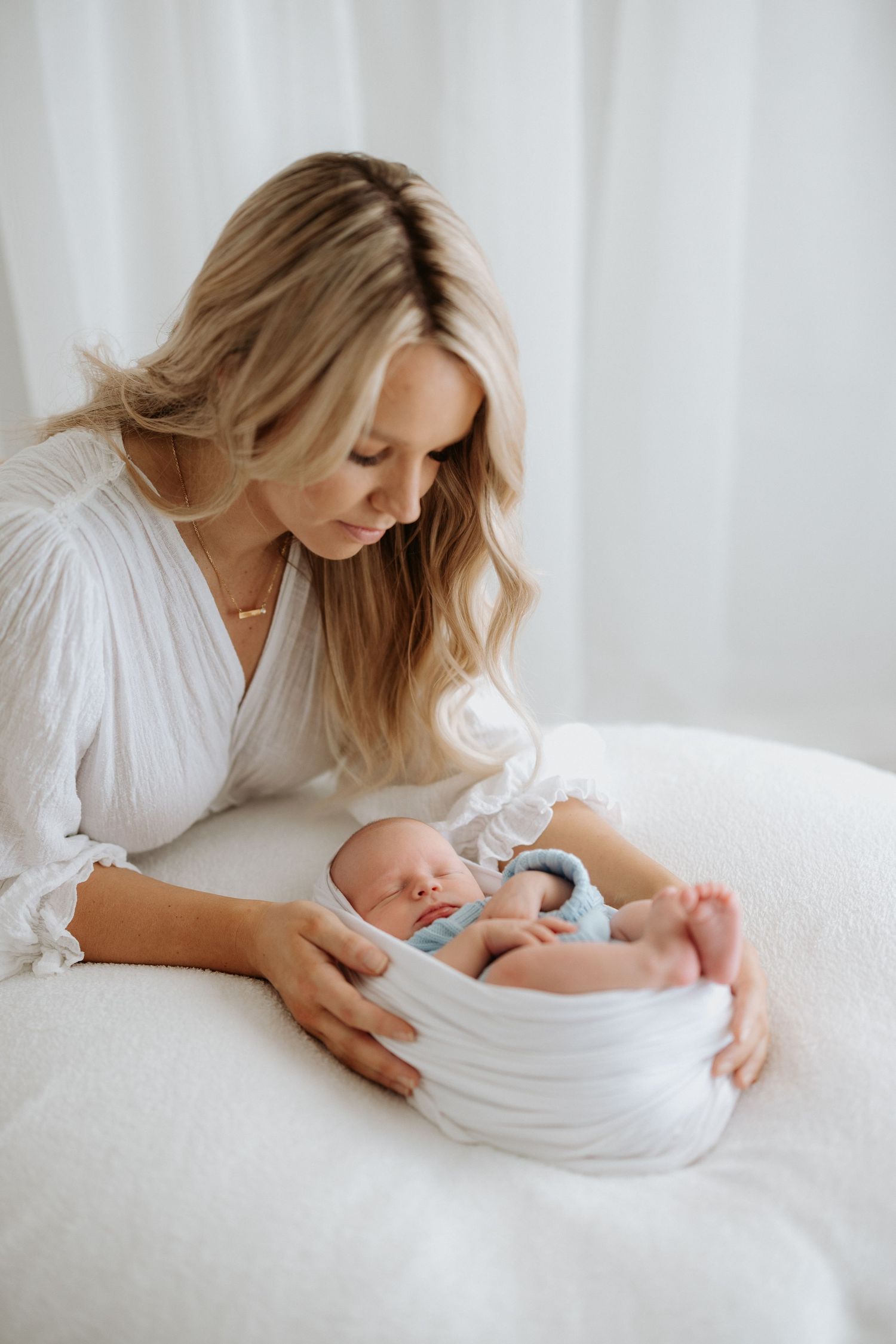 A newborn baby rests peacefully in a white basket while being watched over.
