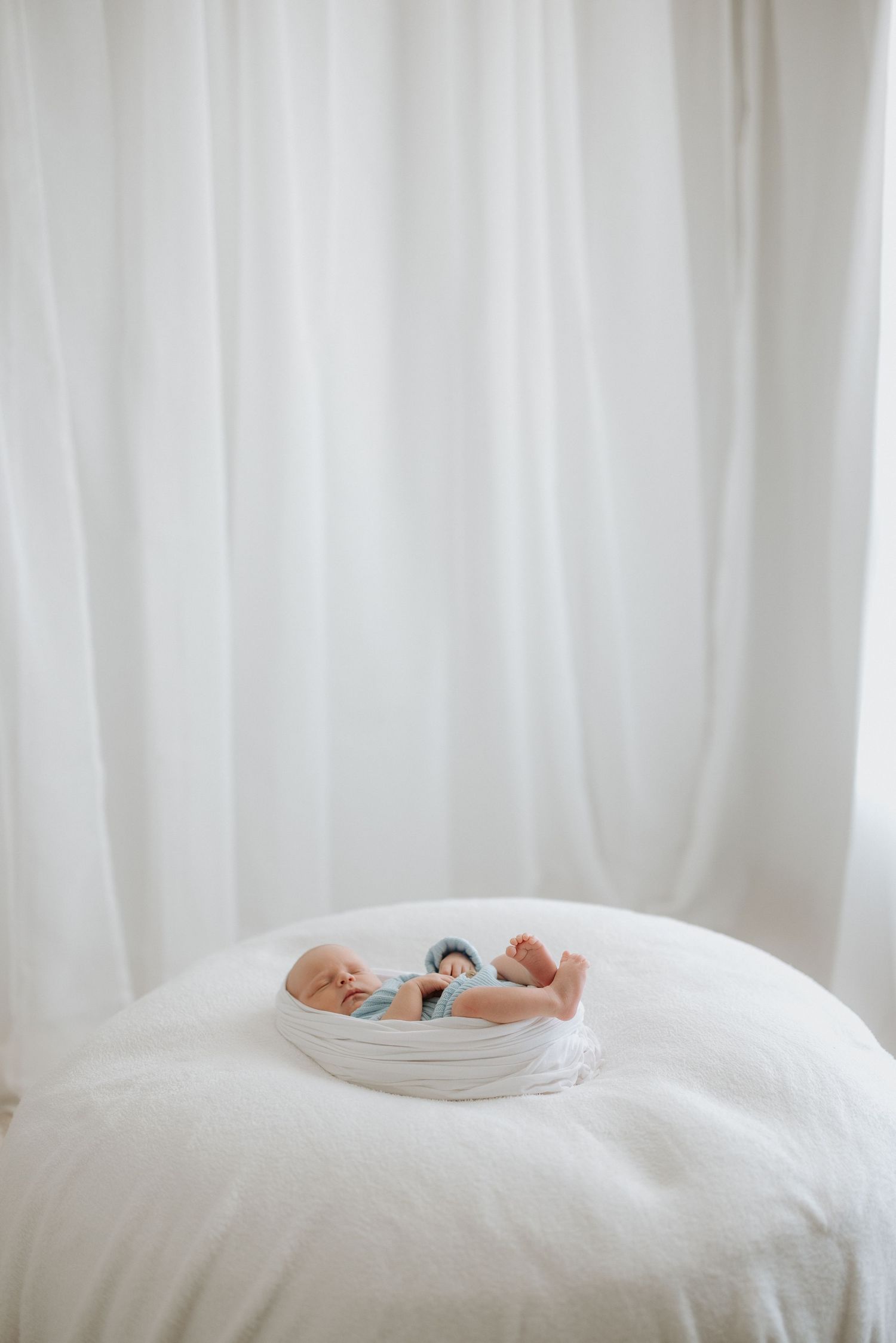 A sleeping newborn baby nestled in a white basket against a light background.