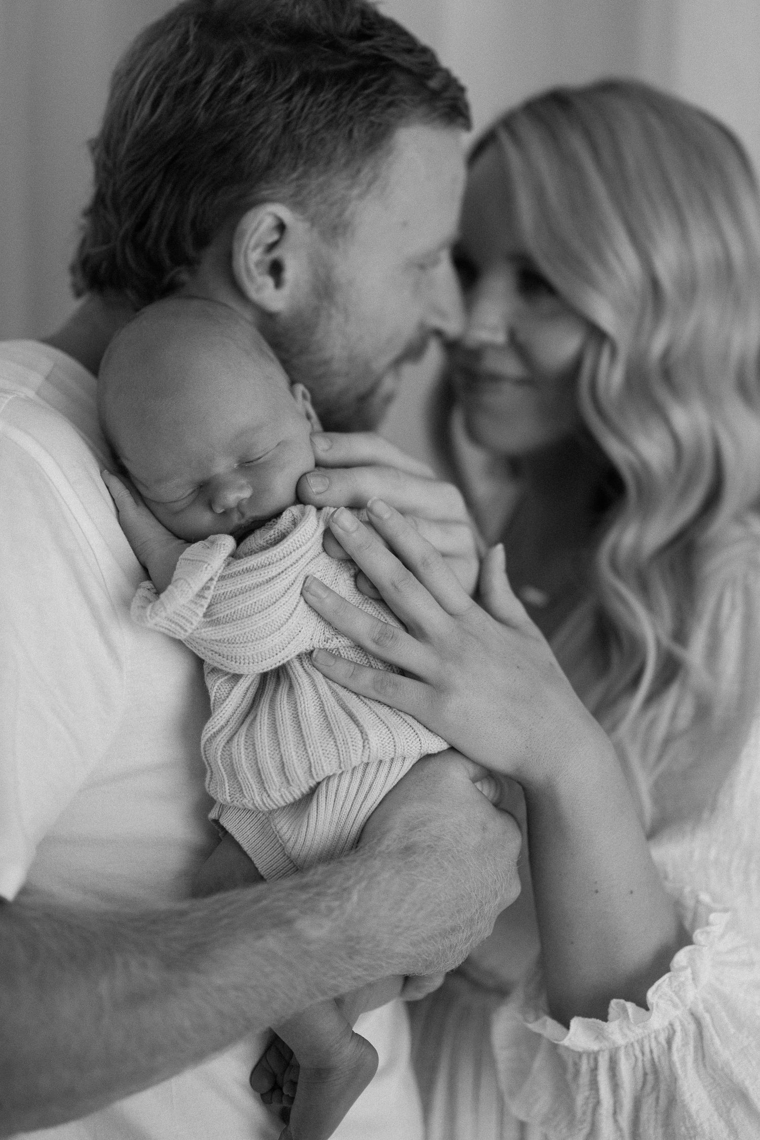 A tender black and white portrait of parents cradling their newborn baby in a gentle embrace.