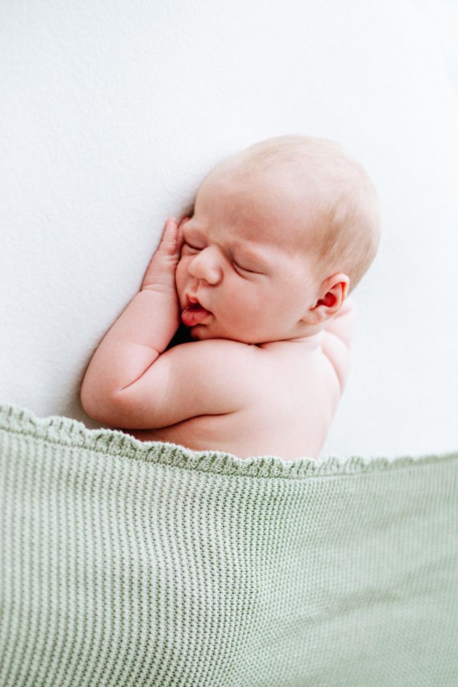 A sleeping newborn rests peacefully against a white blanket, swaddled in cozy knit fabric.