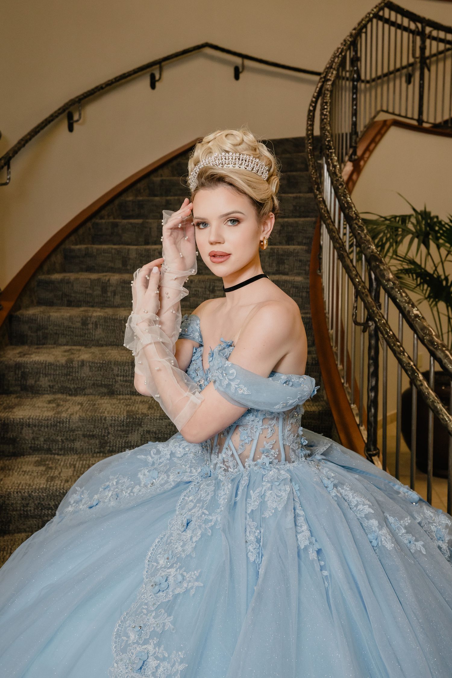 A powder blue ball gown with lace details and off-shoulder design is posed on an elegant curved staircase.