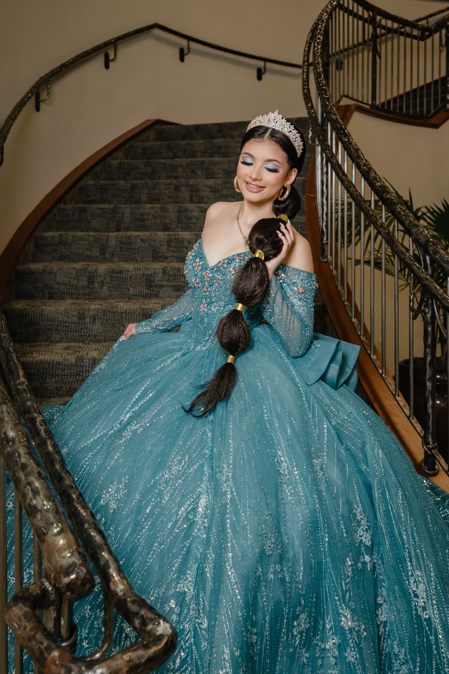 A sparkling turquoise ballgown with glitter details is showcased on an elegant curved staircase.