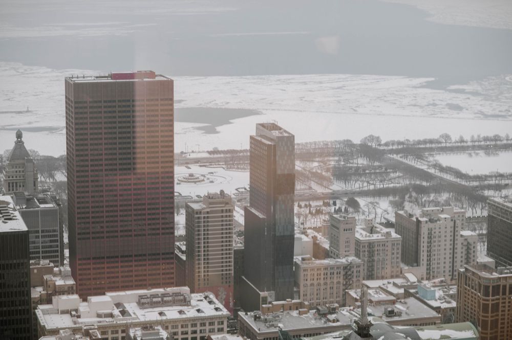 Aerial view of snow-covered downtown Chicago with modern skyscrapers rising against a cloudy winter sky.