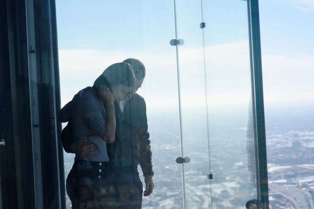A person looks down at a city through the glass floor of an observation deck, high up in a building.