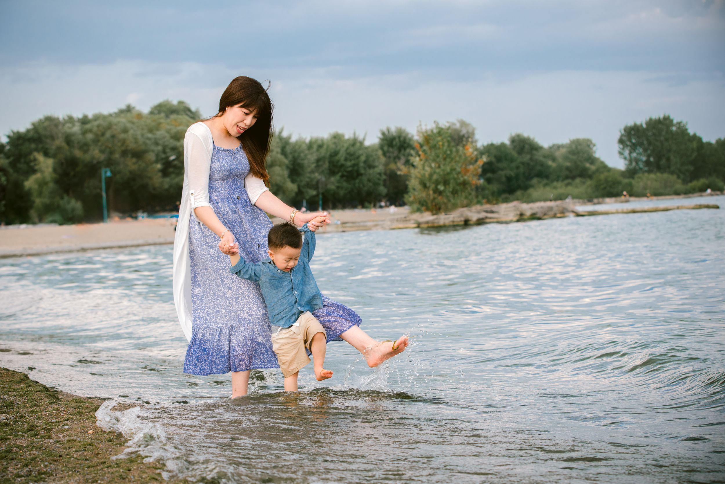 Two people in blue outfits playing at the edge of a lake on a sunny day as gentle waves lap at the shore.