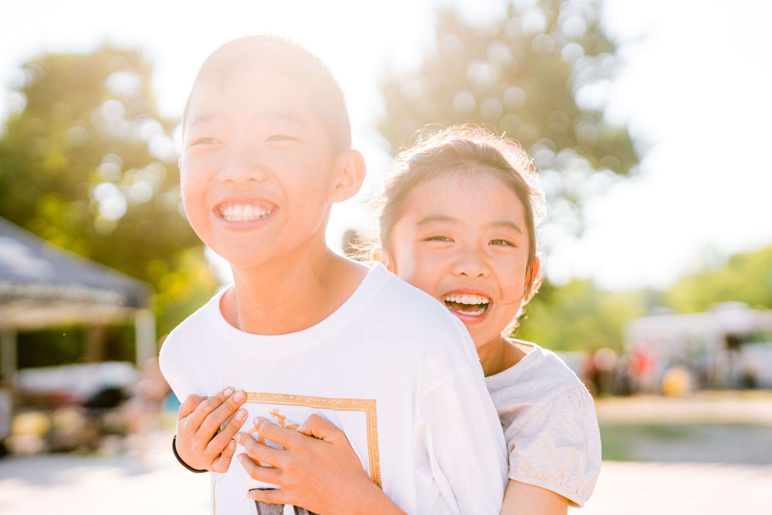 Two joyful friends share genuine laughter while playing together in bright sunlight.