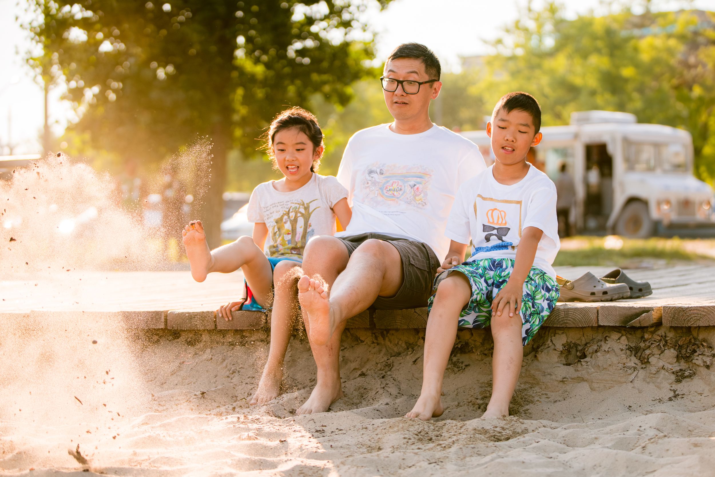 Three people sit on concrete wall at beach during golden hour sunset.