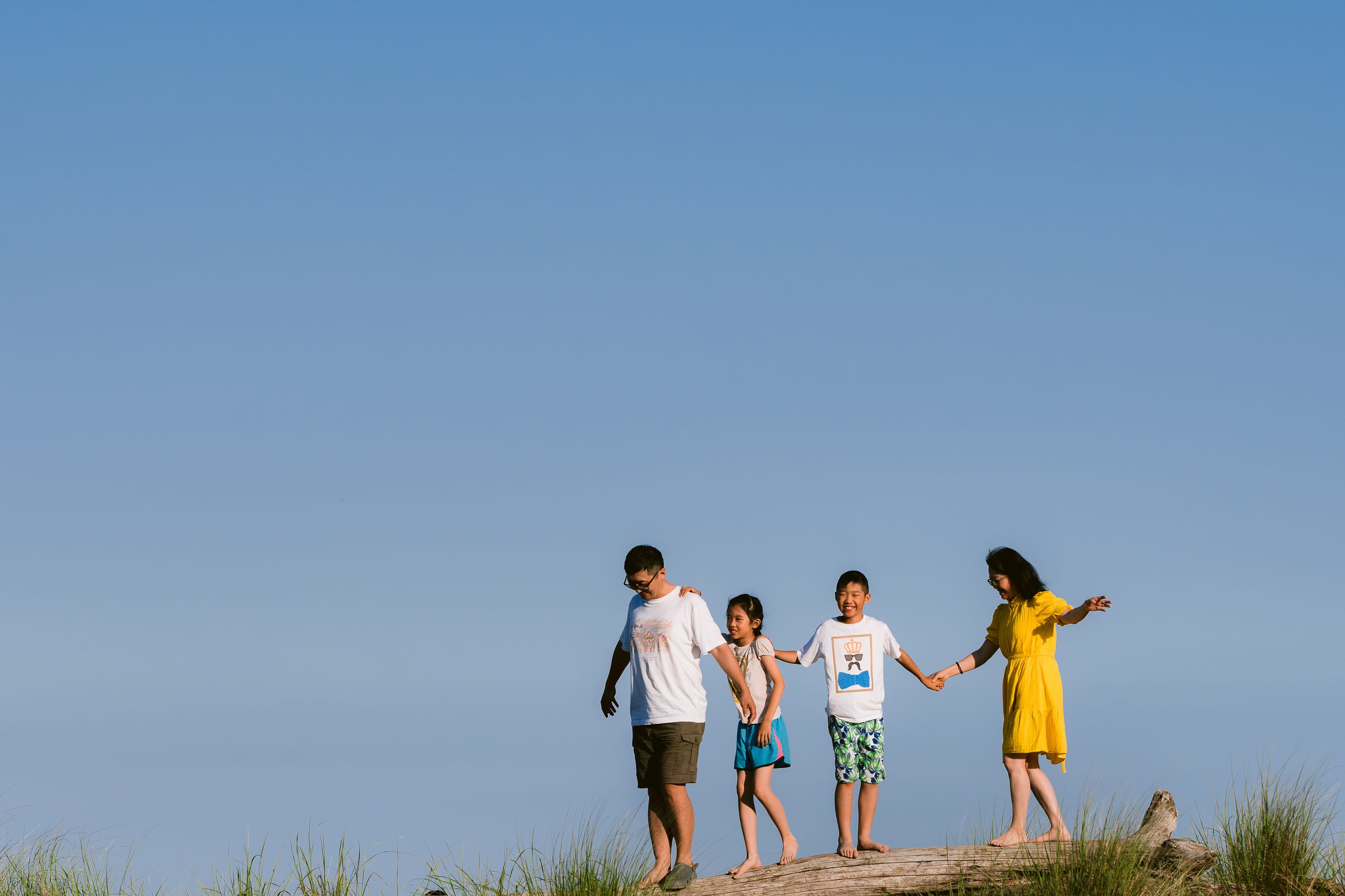 A family walks together on a sandy hill against a bright blue sky during a summer day.