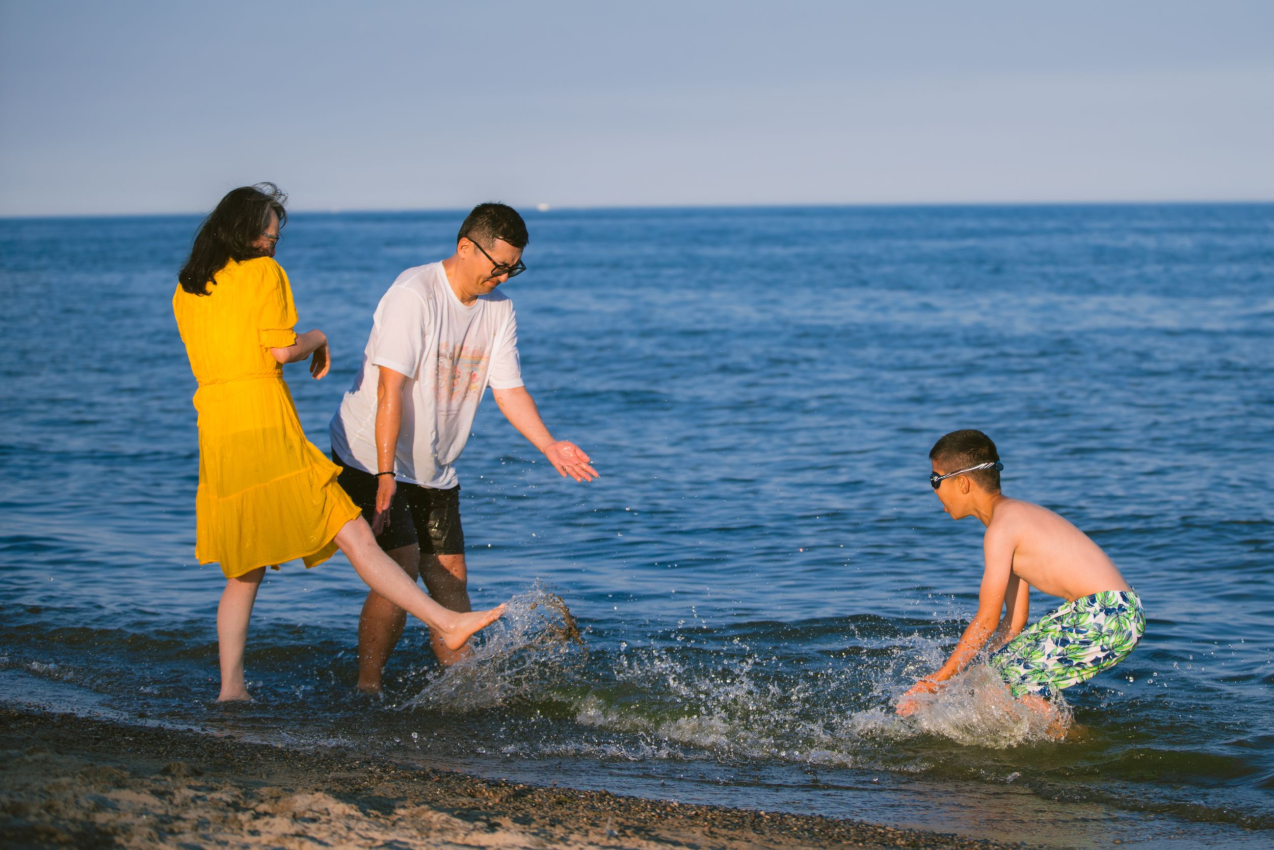 Three people splash and play together in shallow ocean water on a sunny day at the beach.