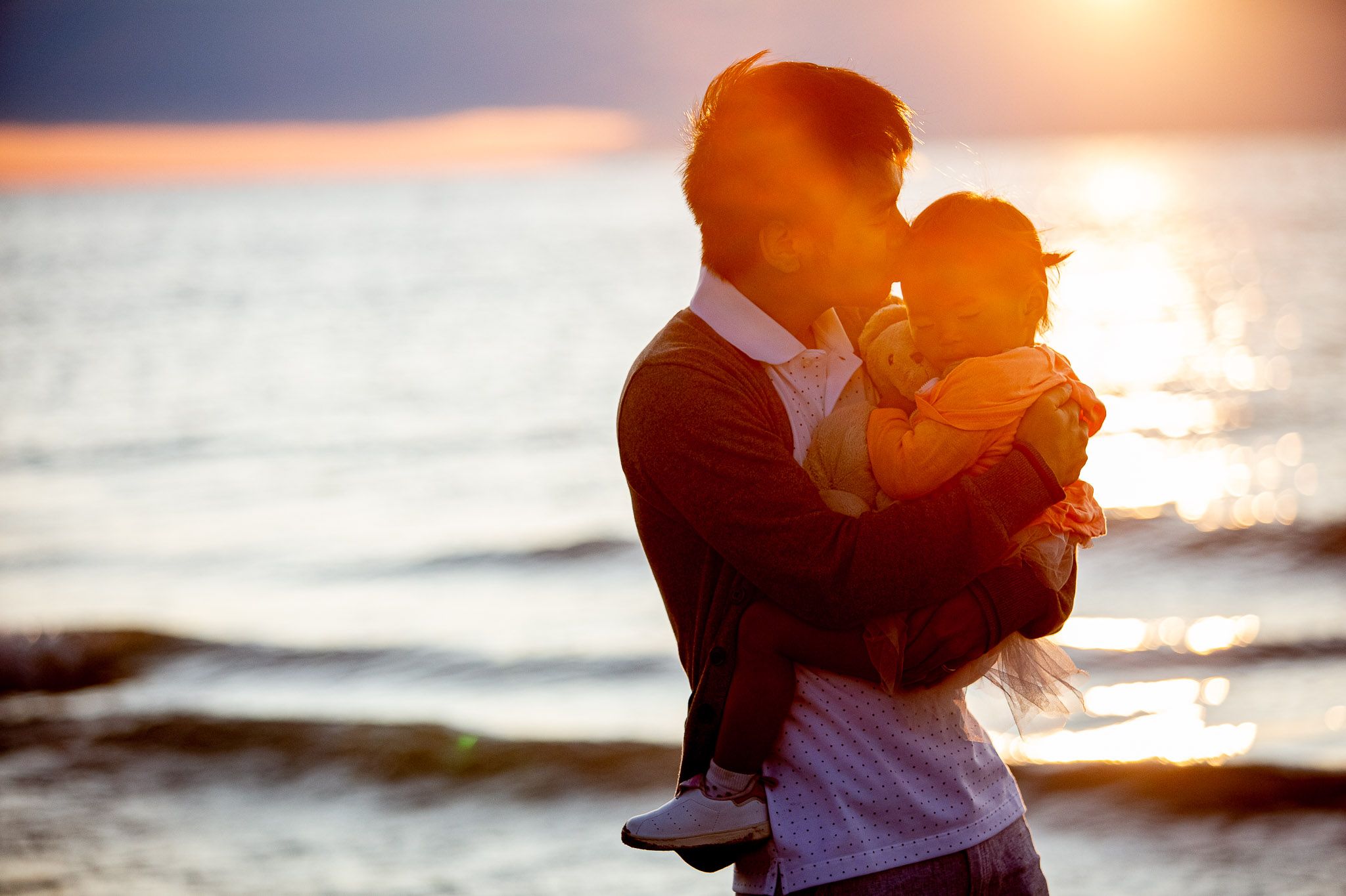 Silhouetted figures embrace on beach at sunset with golden light reflecting off ocean waves.