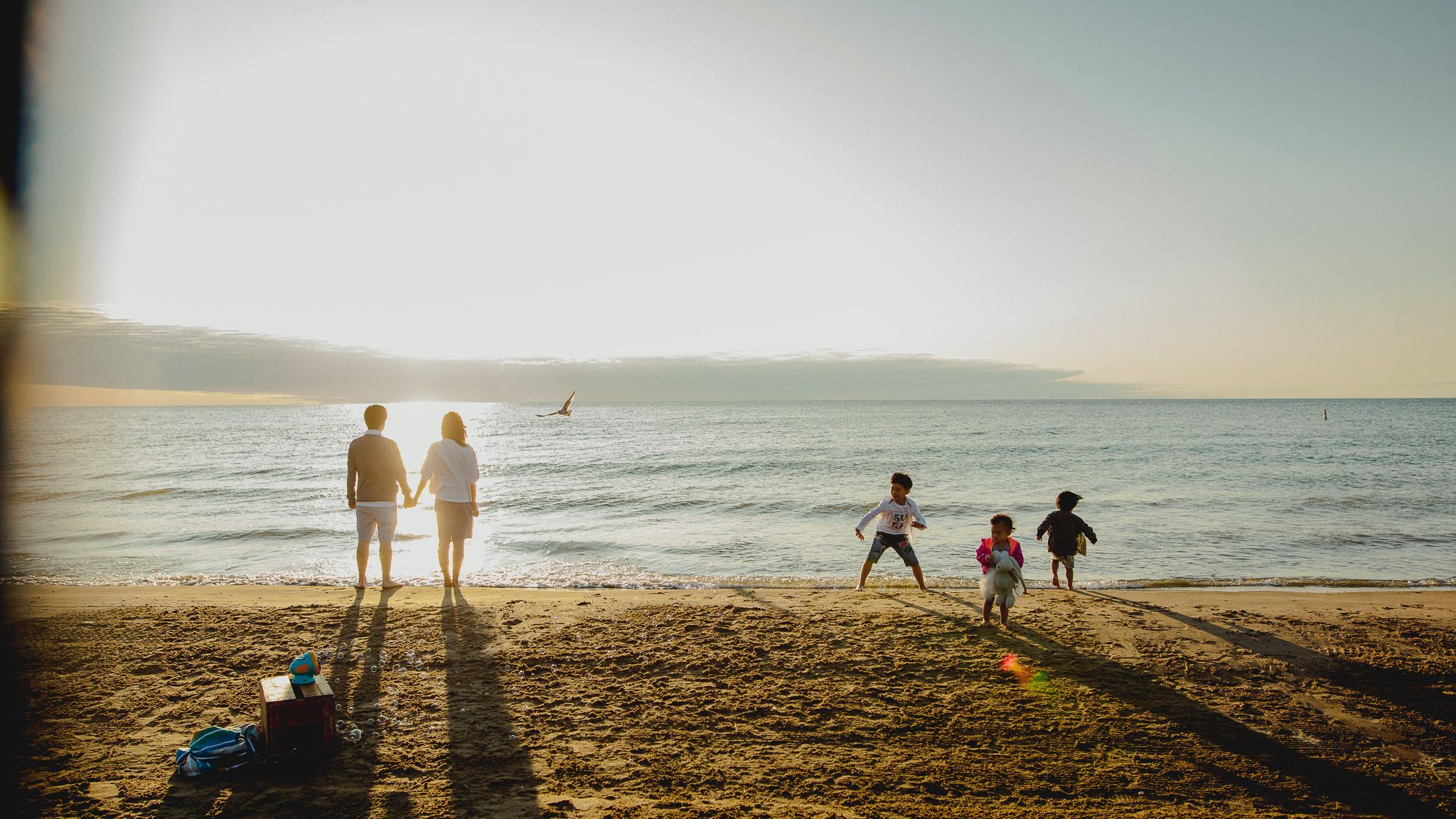 Silhouettes of people enjoying a golden sunset on a beach with mountains in the background during a summer evening.