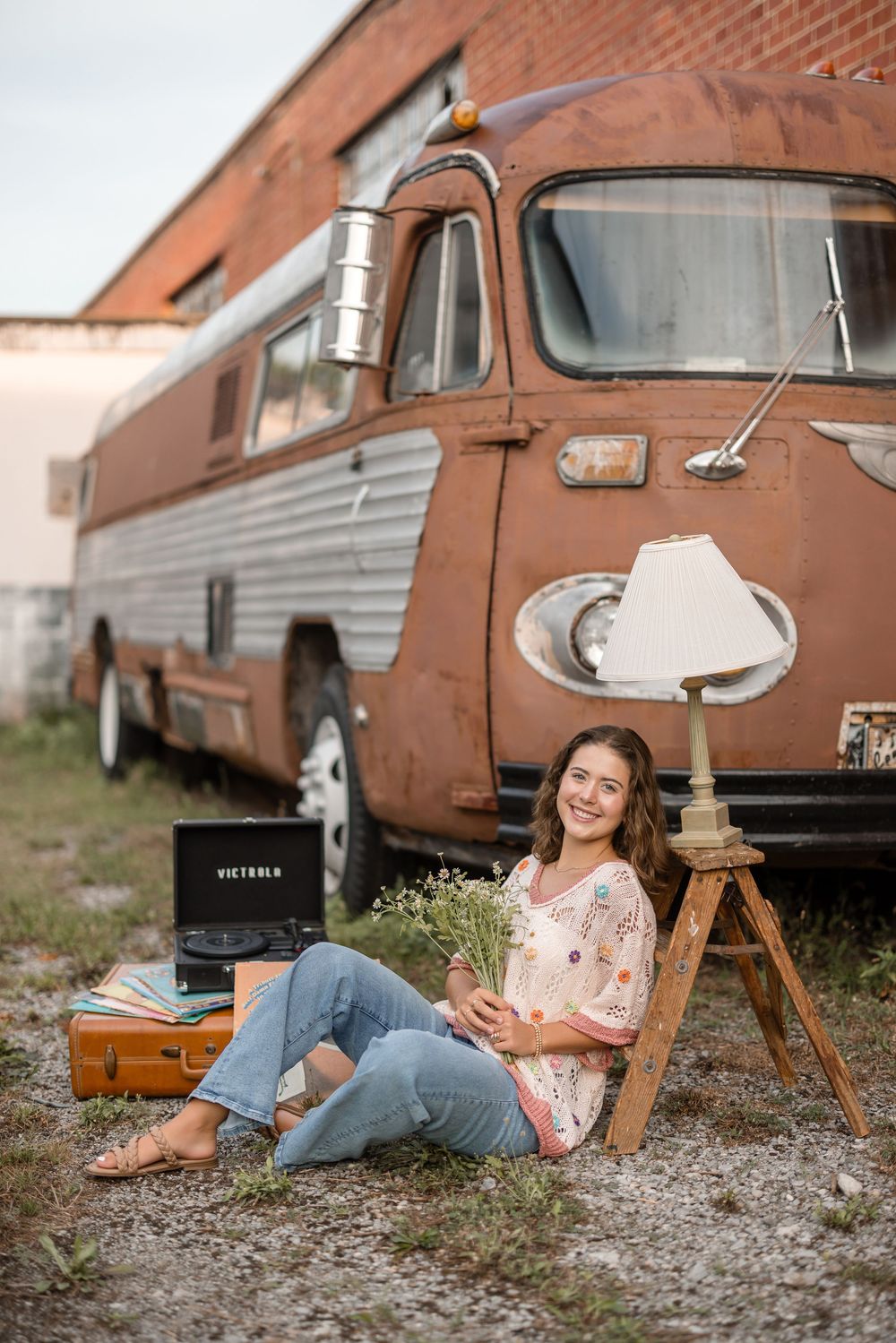 A person relaxes on the ground with a record player and vintage lamp next to a retro orange RV camper van.