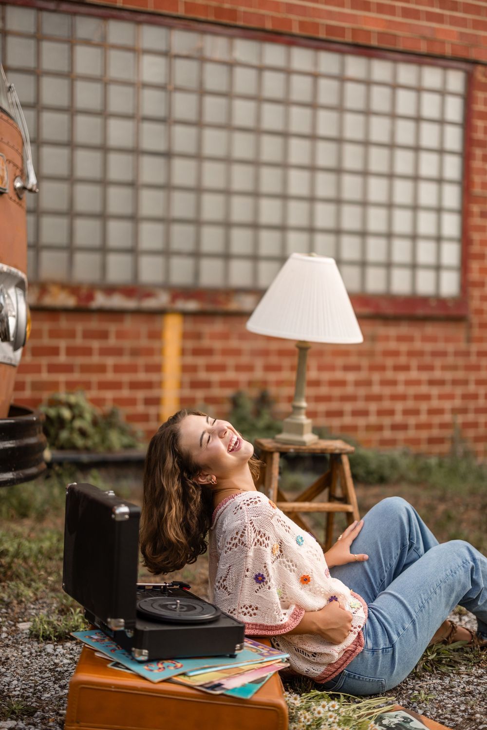 A person relaxes on blankets reading outdoors against a brick wall with laughter and joy.