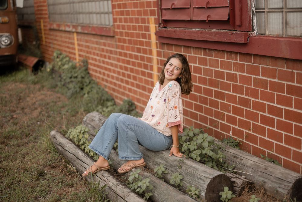 Someone relaxes on a wooden bench against a brick wall wearing a flowy top and jeans on a sunny day.