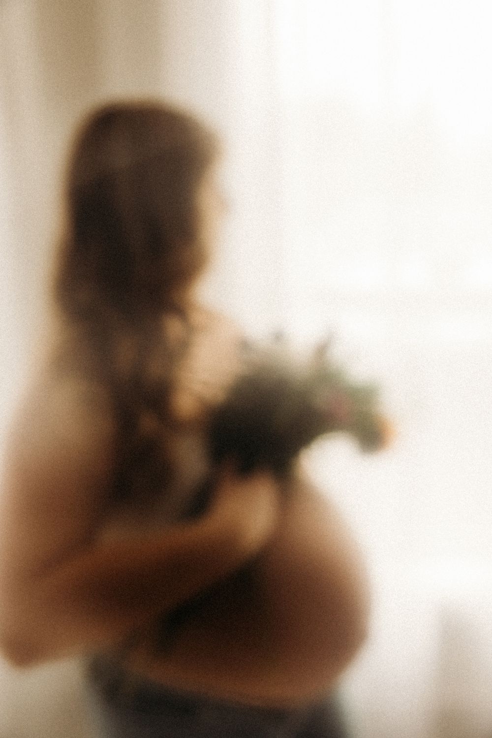 Dreamy sepia toned maternity portrait with woman holding bouquet.