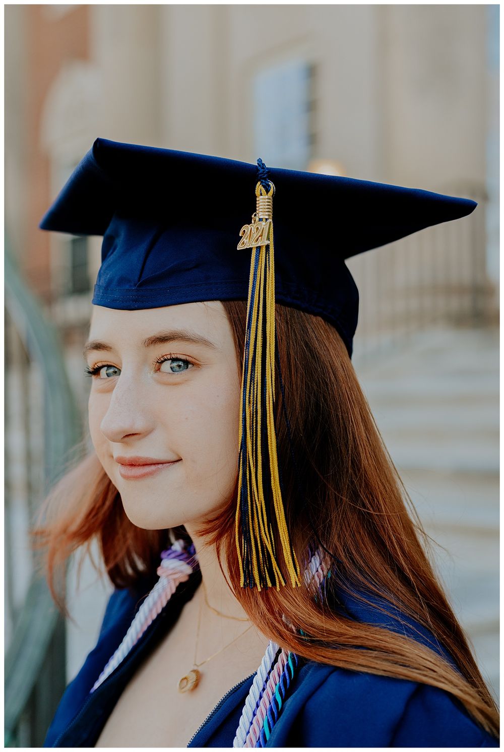 Graduate wearing blue cap and gown with gold tassel against stone building.