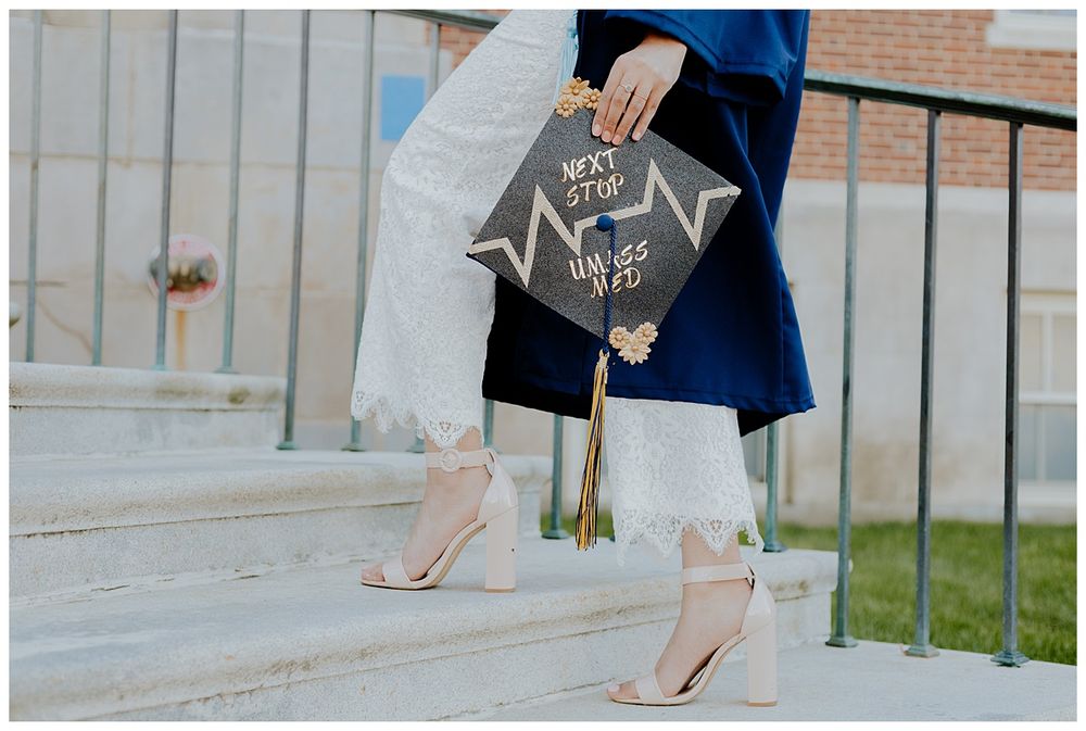 Close-up of decorated graduation cap and white heels on concrete steps.