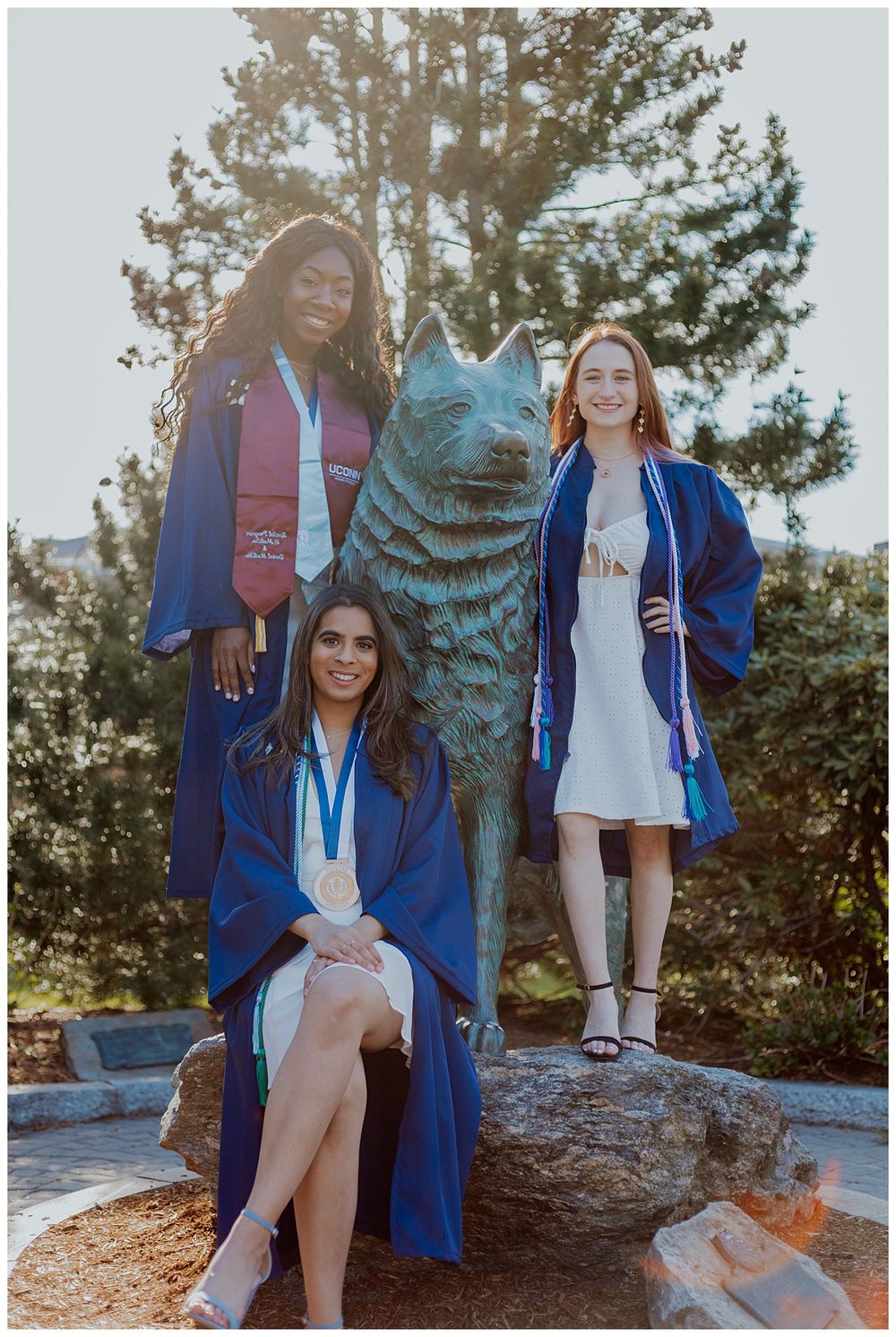 Three graduates pose with the UConn Husky mascot statue during commencement celebrations.