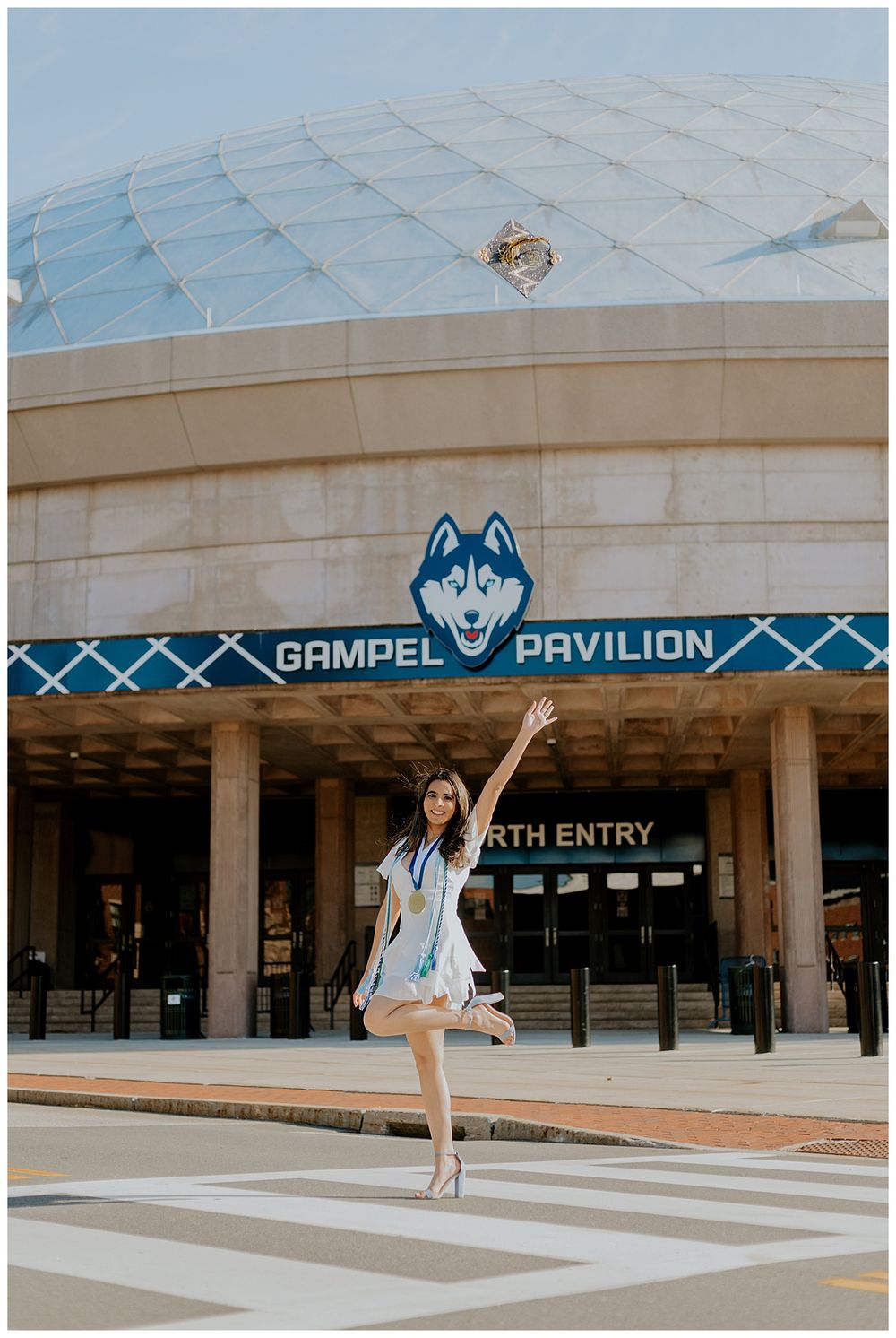 Graduate strikes a pose in front of the Gampel Pavilion at UConn during commencement.