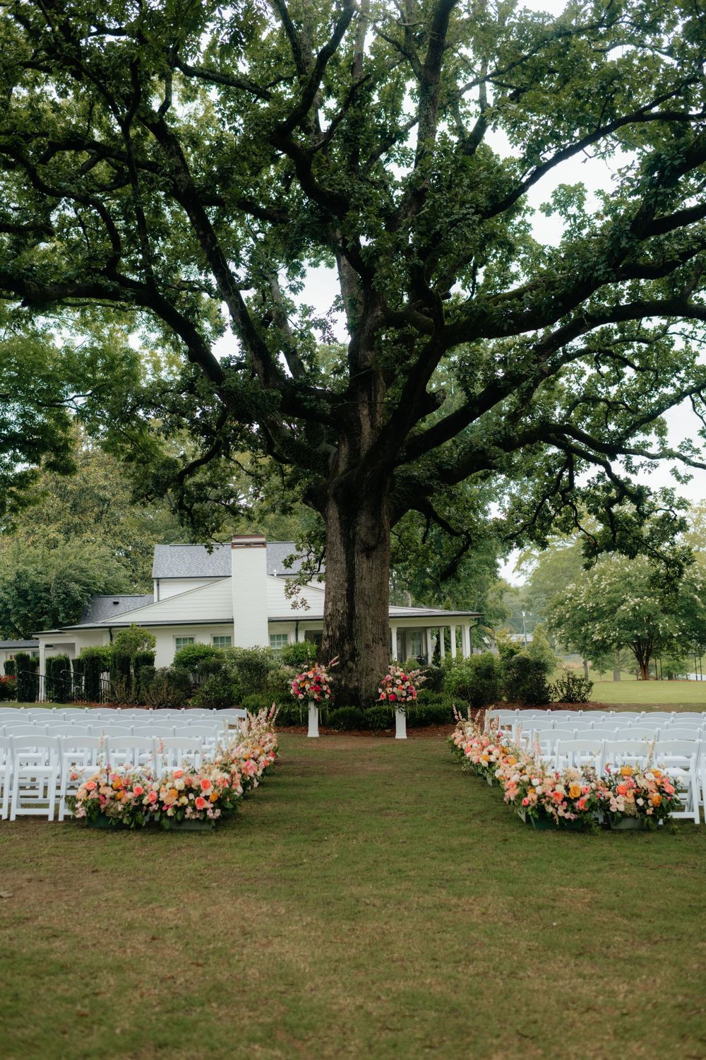 a view of a rainy wedding ceremony set up under a live oak in the backyard of the lumpkin house wedding venue, in albertville, alabama.