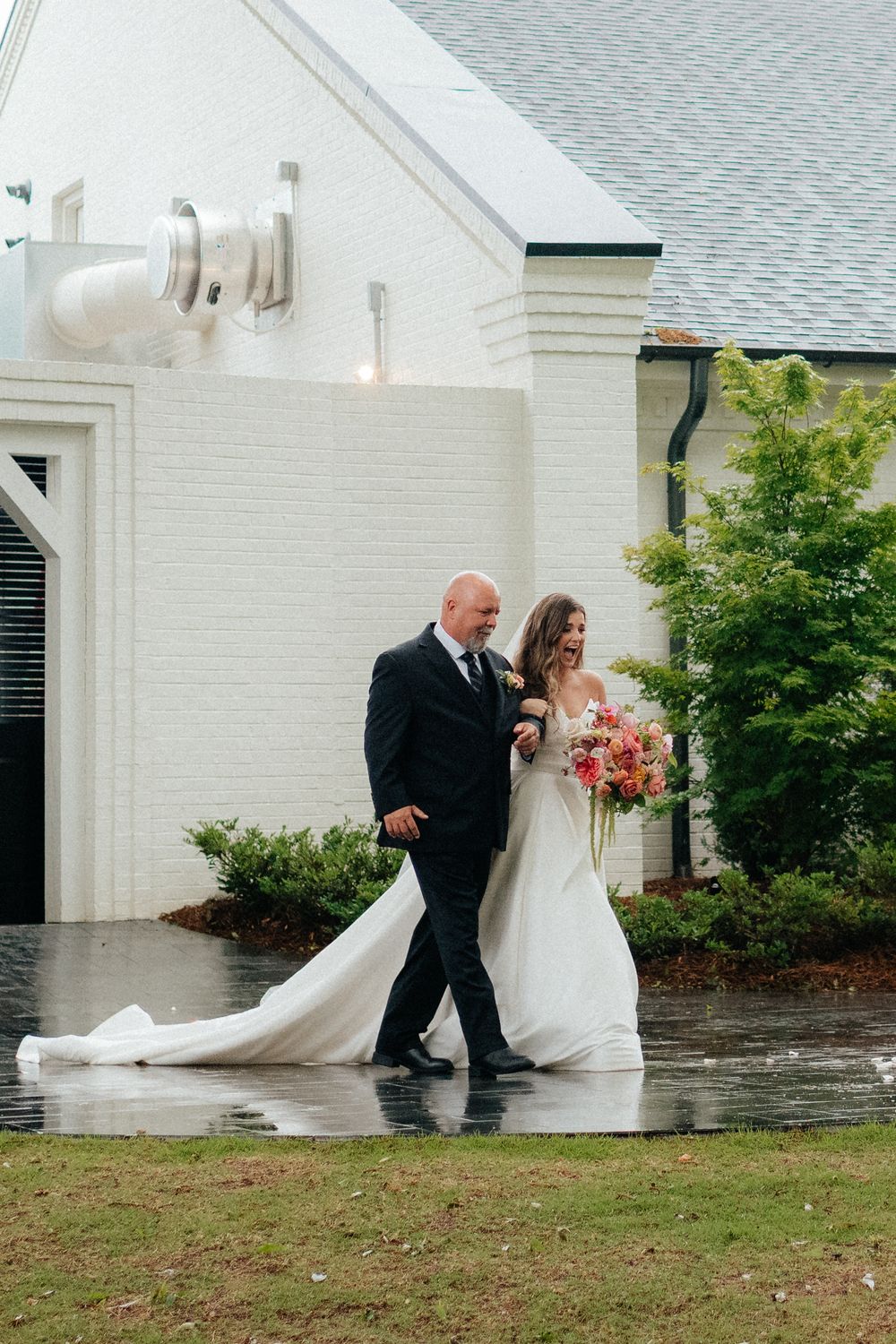 a bride and her father walk through the rain to her outdoor wedding ceremony in the backyard of the lumpkin house venue in albertville, al