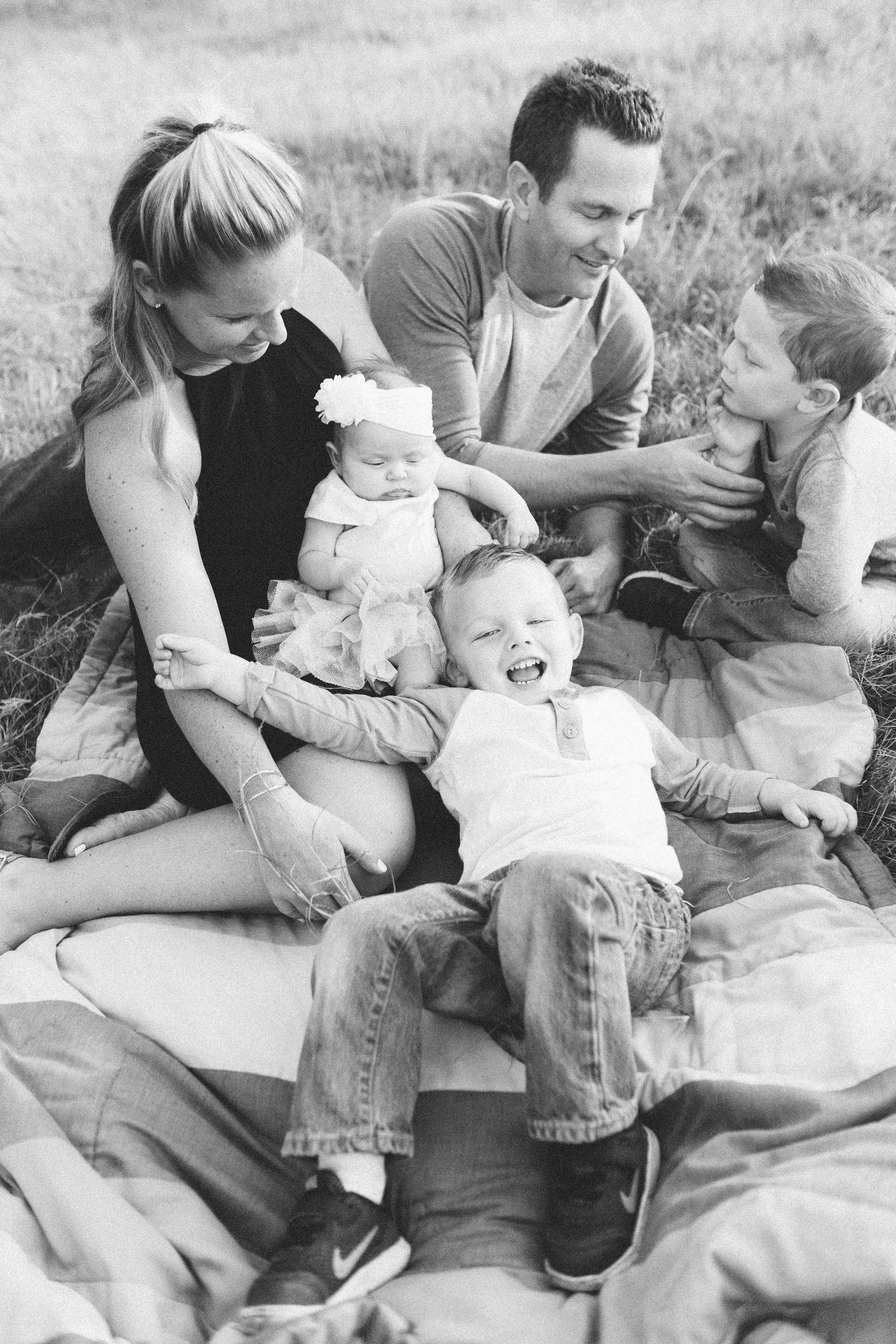 family sitting on a blanket on the grass, black and white