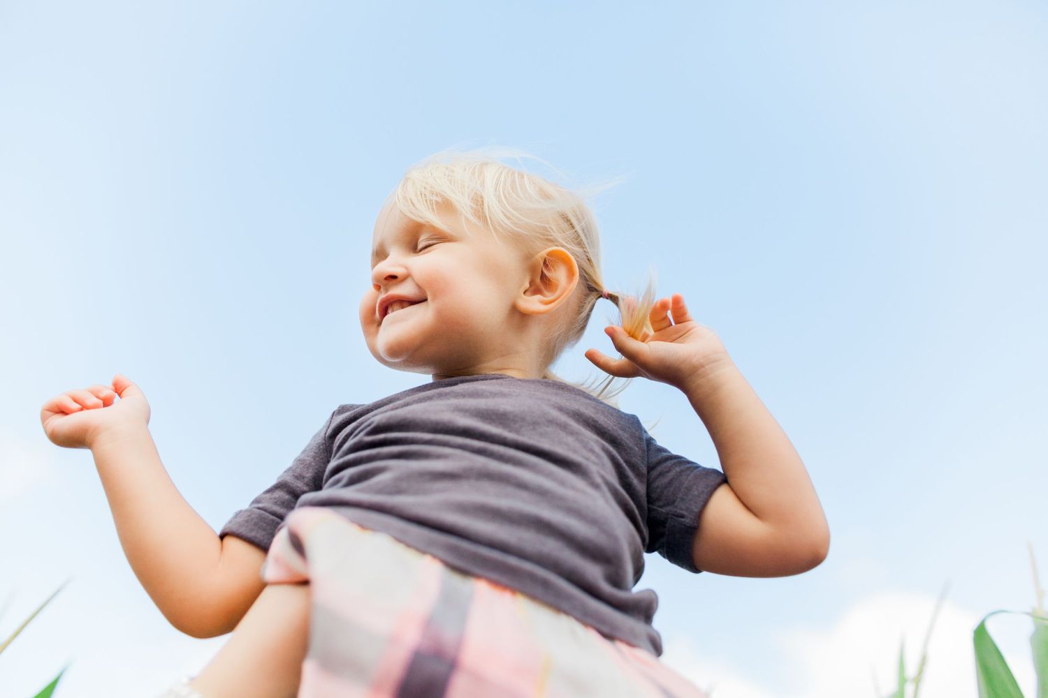 little girl closing her eyes being held up in the air, just sky behind her