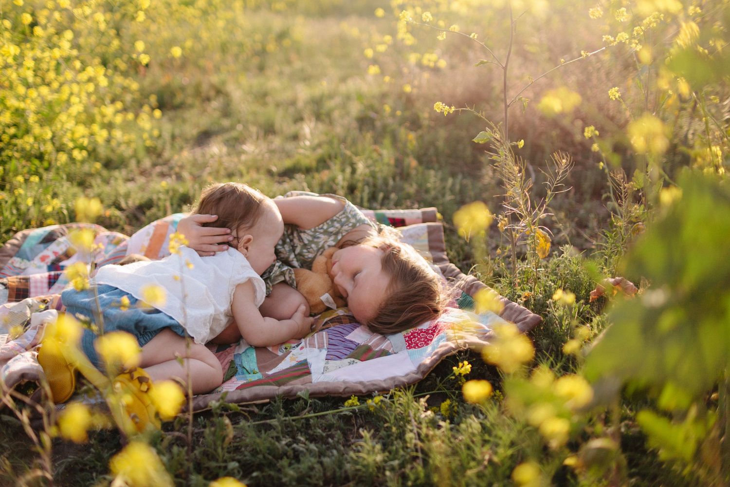 little girl and toddler sister laying on a blanket in a field of wildflowers