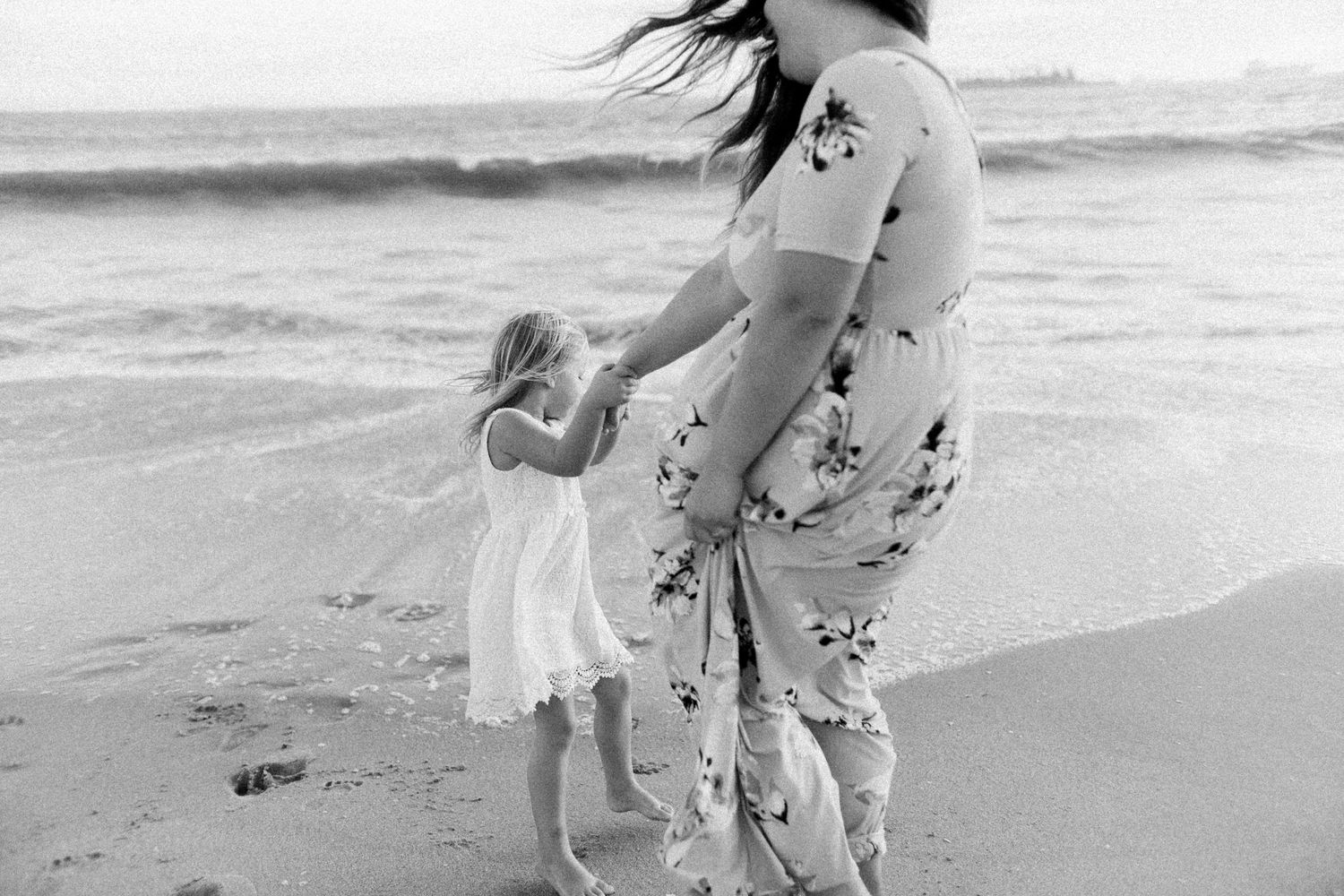mom and daughter at the beach, daughter leading mom to the water. black and white