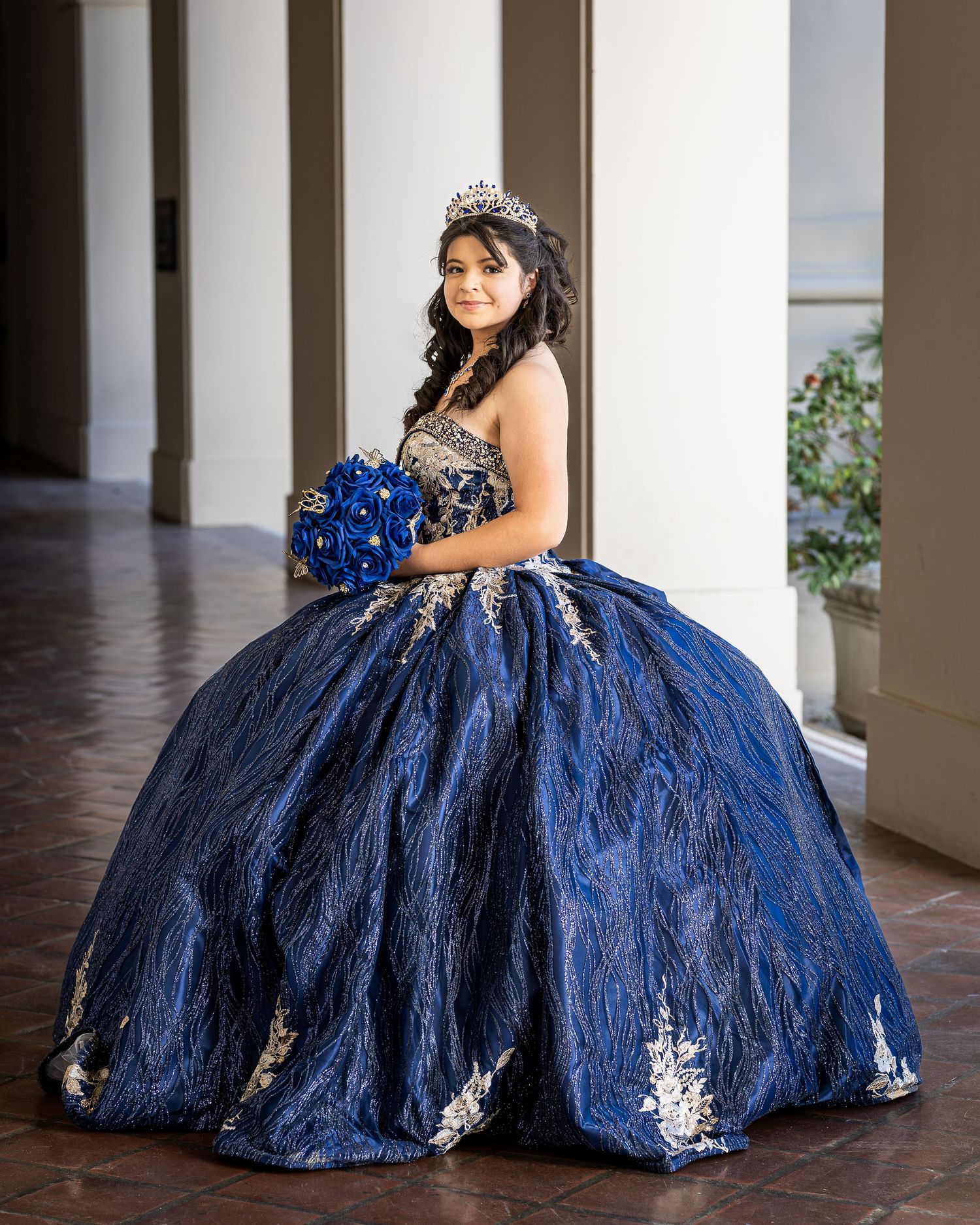 A glamorous quinceañera dress in navy blue with intricate details sparkles in an elegant colonnade setting.