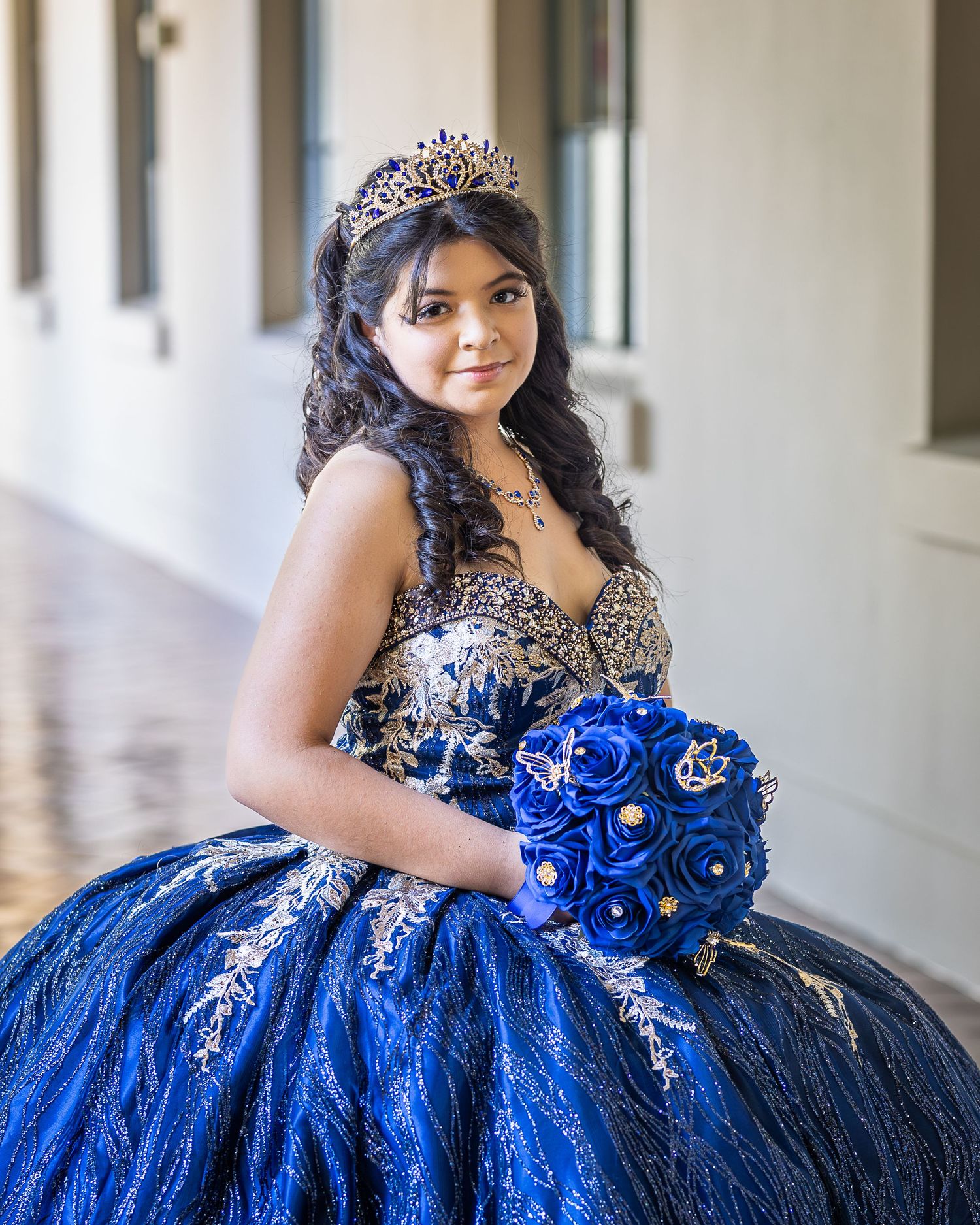 Traditional quinceañera gown featuring deep blue roses and silver sequined details against dark tulle fabric.