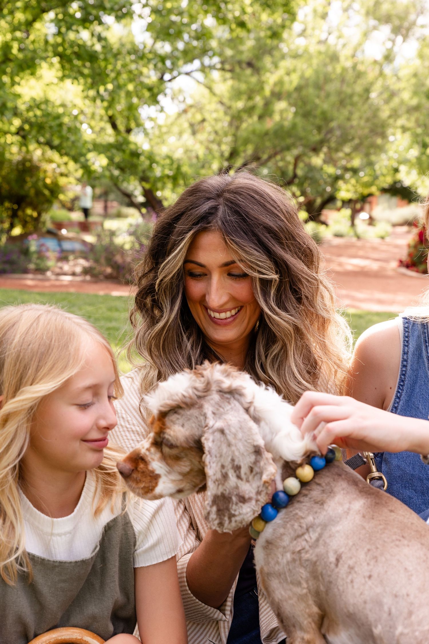 a cute dog with white and brown fur is surrounded by 2 Kids and a mom lovingly playing together