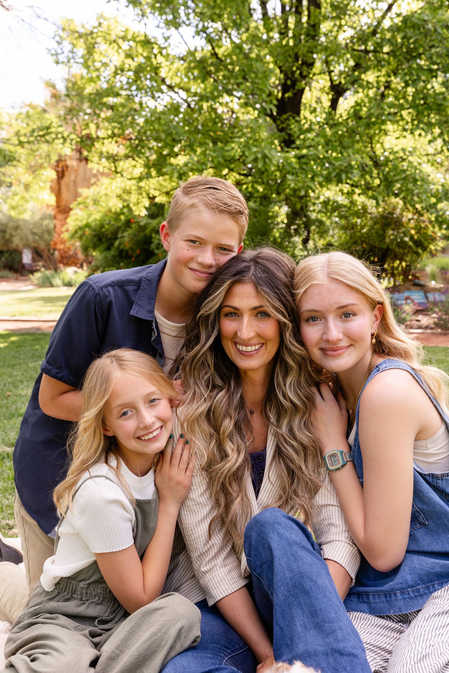 mom with beautiful curly long hair sitting with her 2 teenage kids 1 boy 1 girl and 9 year old girl sitting close smiling at the camera