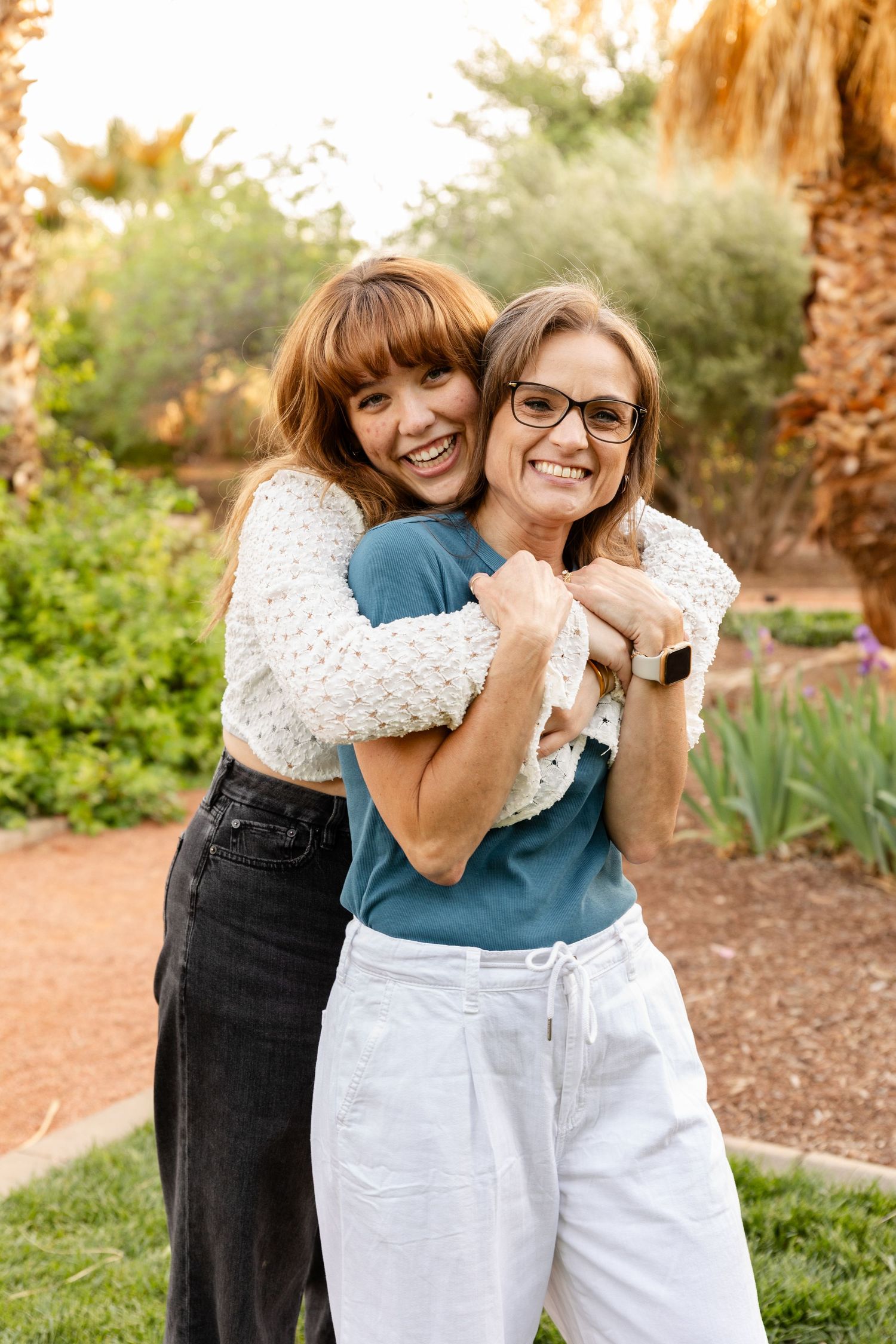 a teenage daughter hugging her mom around her shoulders with trees in the background