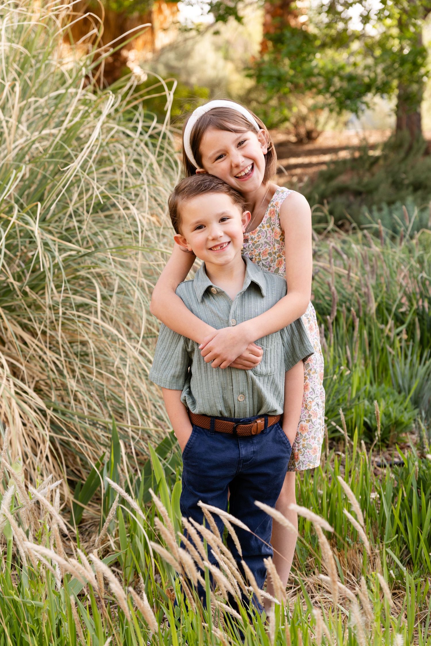an 8 year old girl hugging her 5 year old brother from behind both laughing at the camera fox tails blowing in the wind beside them