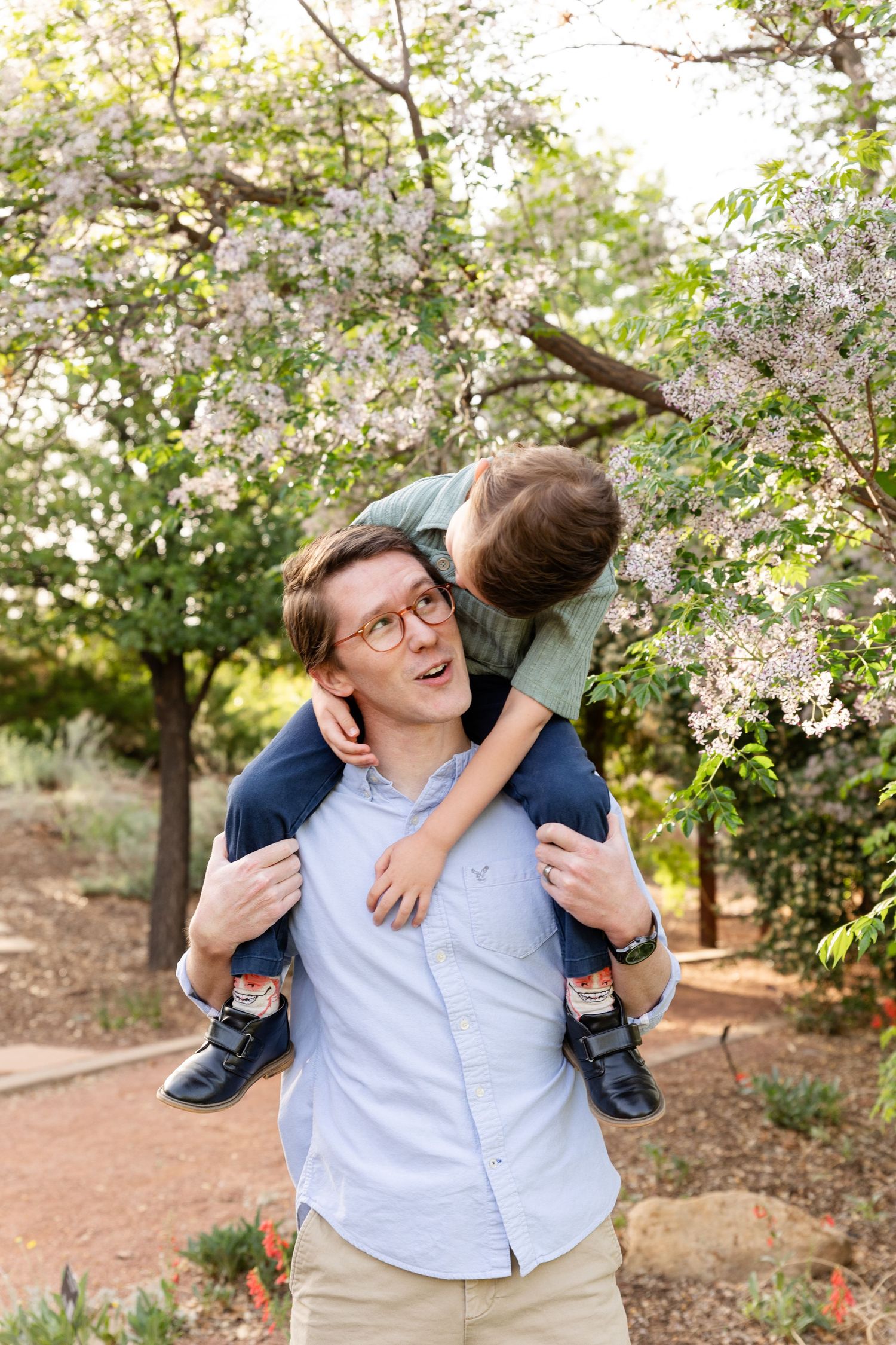 5 year old boy sitting on dads shoulders laughing at each other