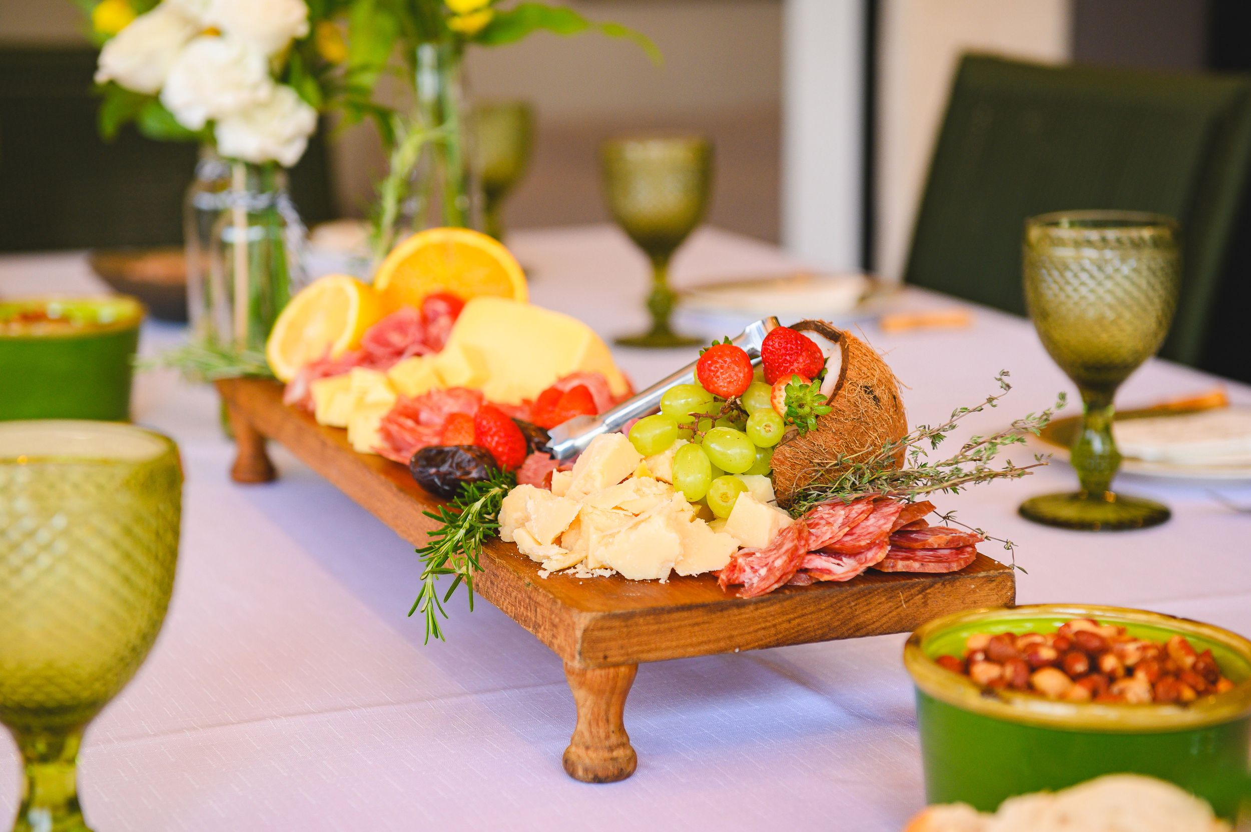 Gourmet seafood appetizers served on wooden boards with fresh garnishes and green glassware on a white tablecloth.