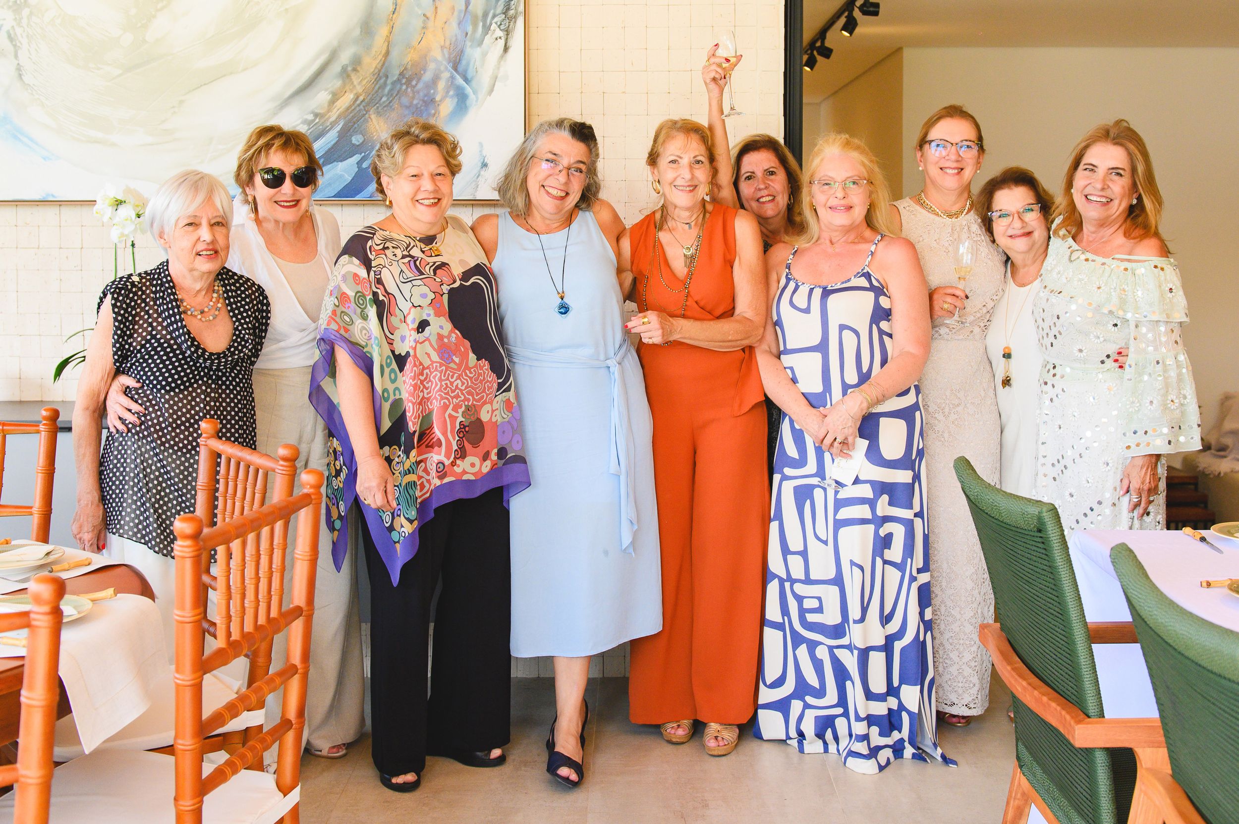 A group of women pose together at a social gathering wearing colorful summer dresses and casual attire.