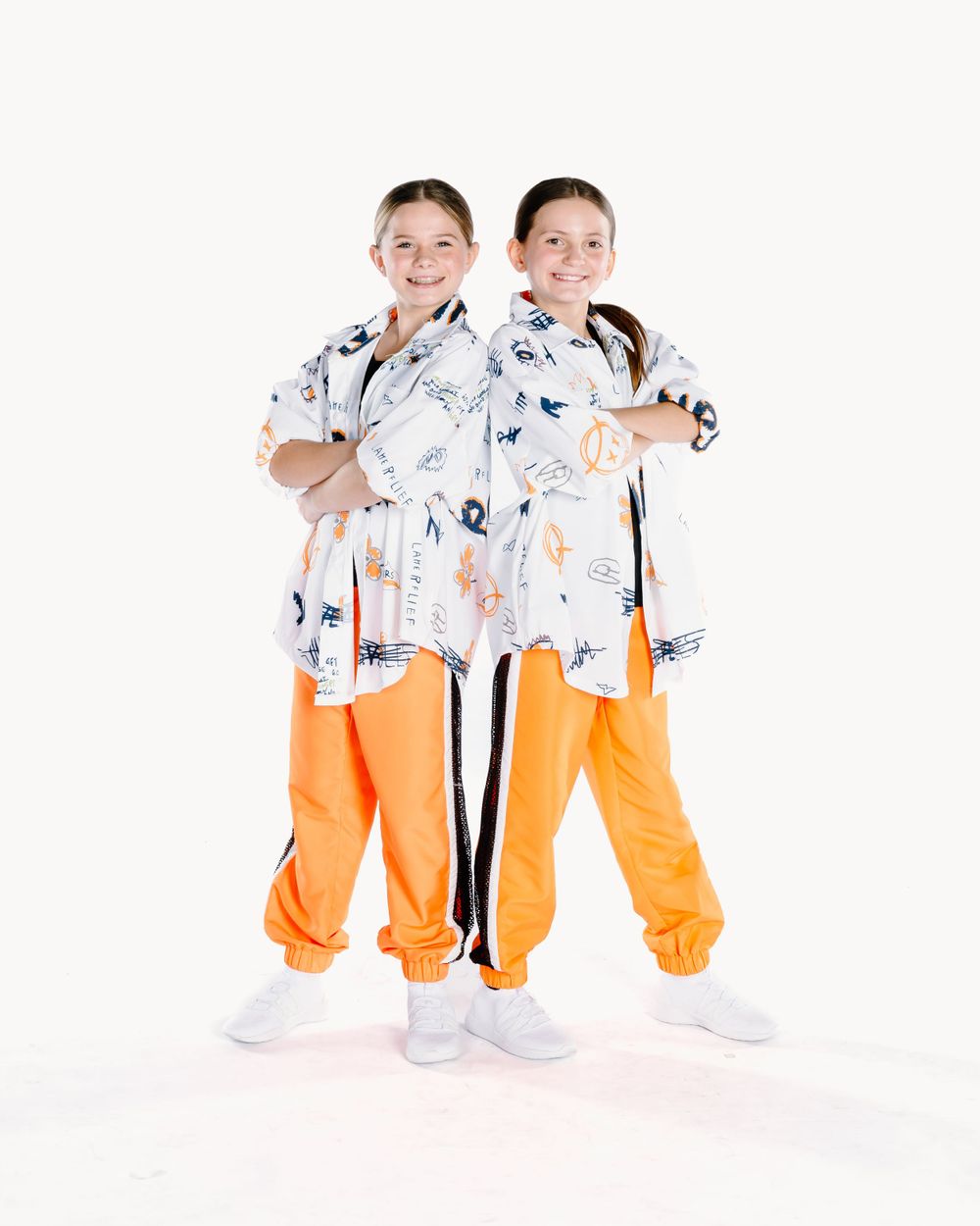Two people wearing matching patterned white shirts and bright orange pants pose back-to-back on a white background.