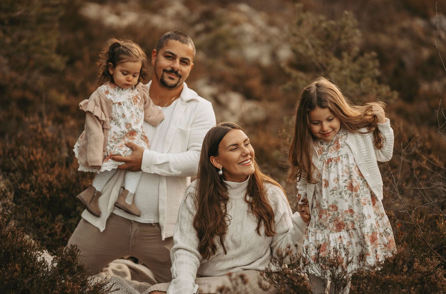 Family in coordinated white outfits sitting together in nature during sunset with warm brown tones.