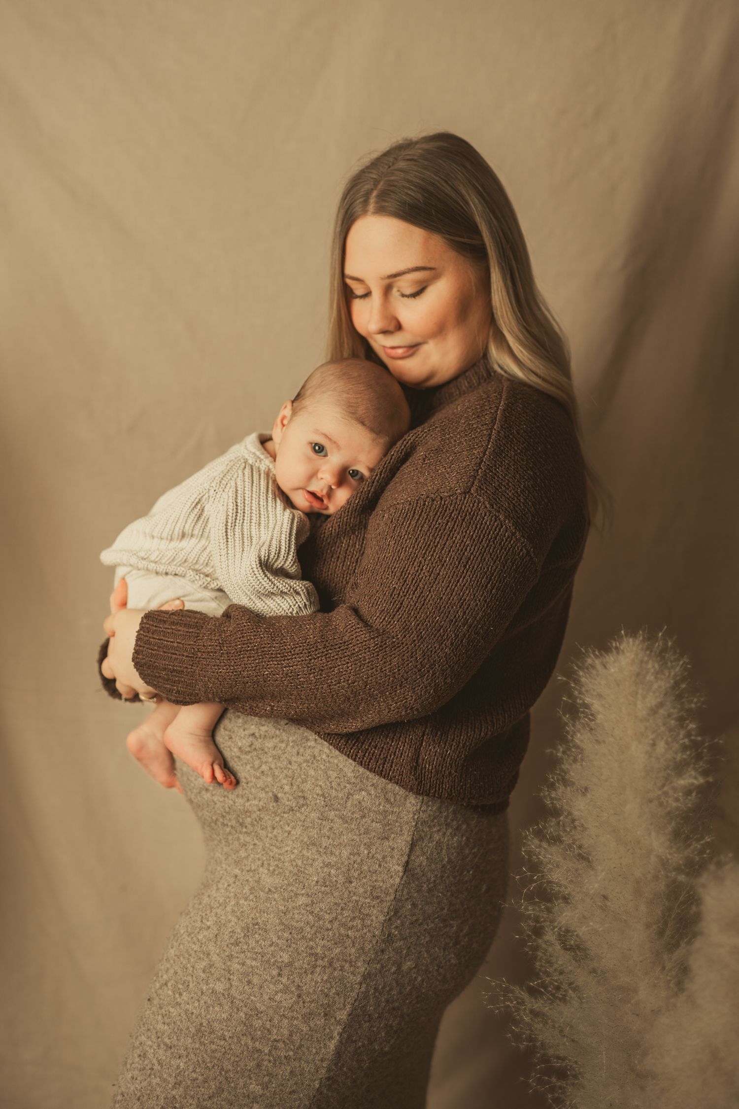 A tender moment captured in warm tones as a parent in a brown sweater embraces a baby in cream-colored clothing.