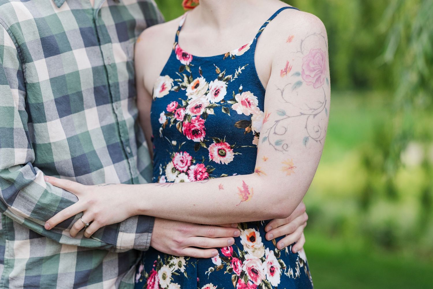 A close-up of arms embracing, showing floral dress details and plaid shirt patterns against a green outdoor background at Cantigny Park