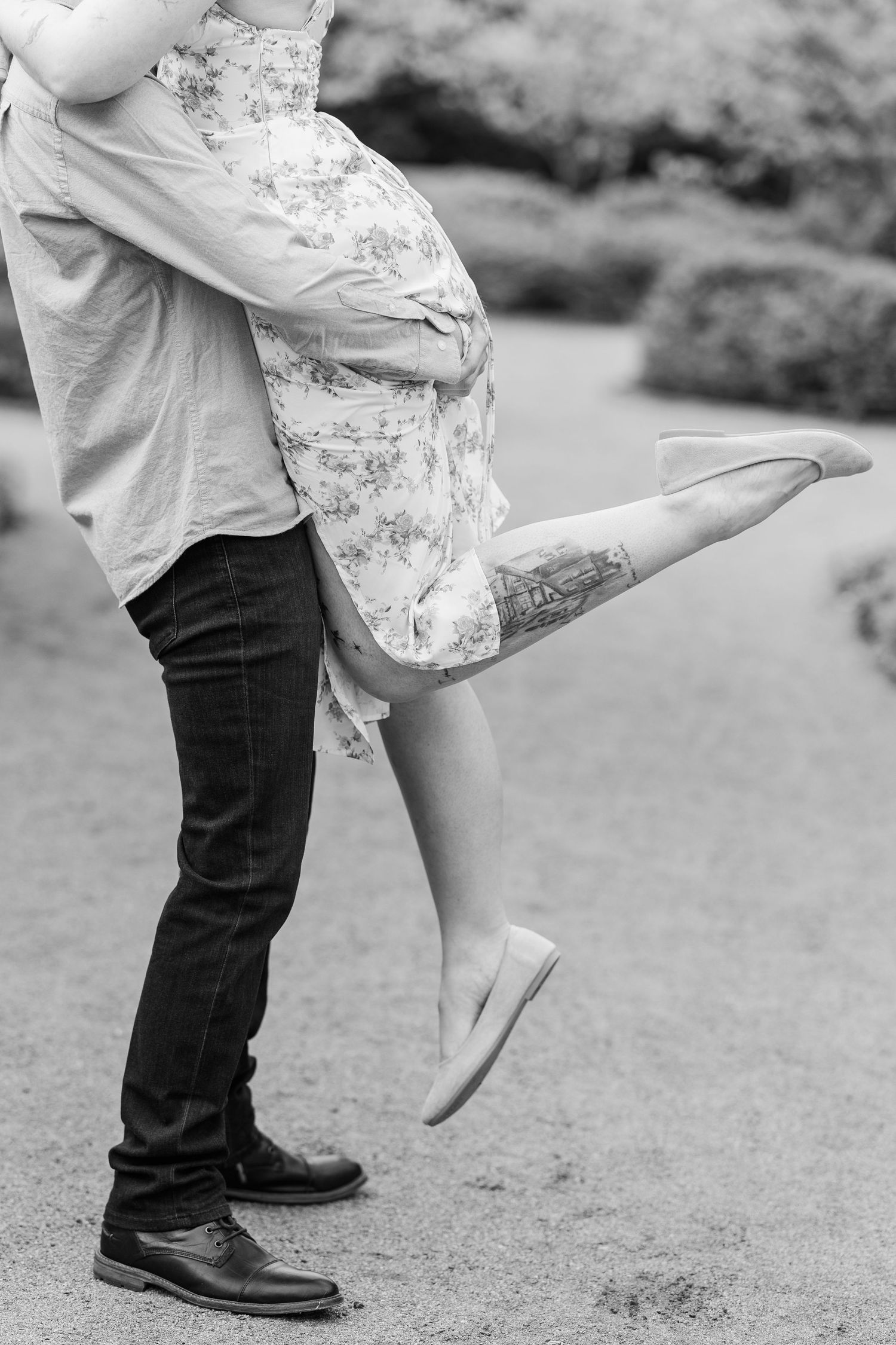Two people in a romantic embrace on a garden path, with floral dress and jeans visible as one person lifts their leg at Cantigny Park