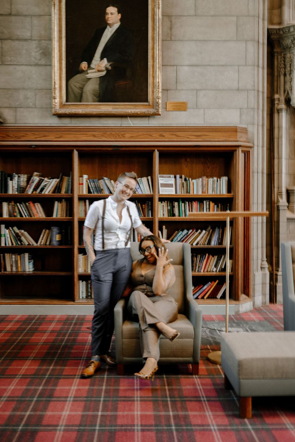 A stylish couple posing together in a library with plaid carpet and vintage decor.