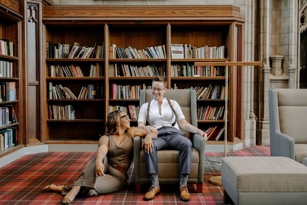 A couple relaxes together in a vintage library room with wooden bookshelves and a red patterned carpet.