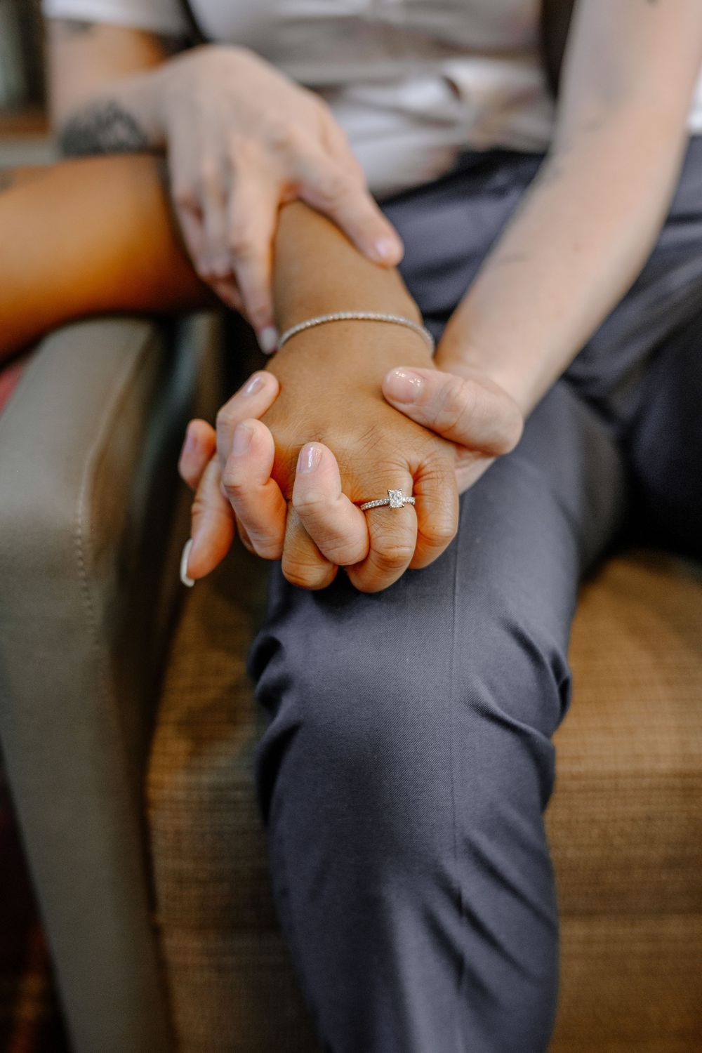 Close-up of two hands holding each other with an engagement ring visible.