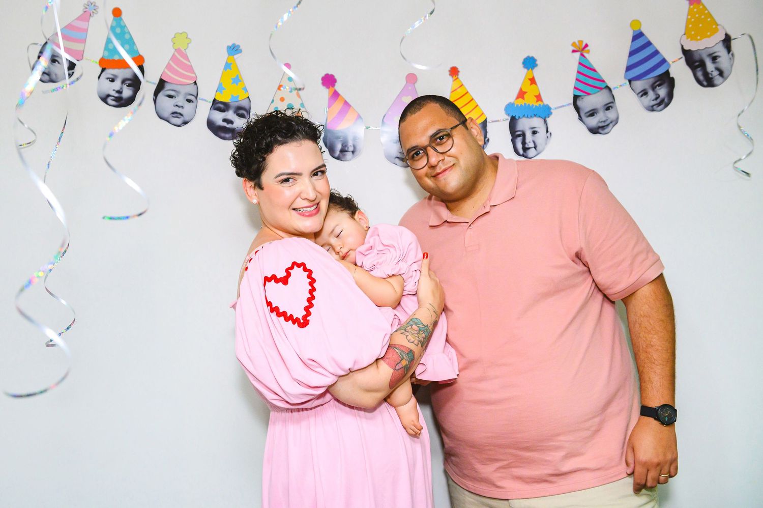 A family poses together at a party with festive decorations and a banner of party hats on a wall behind them.