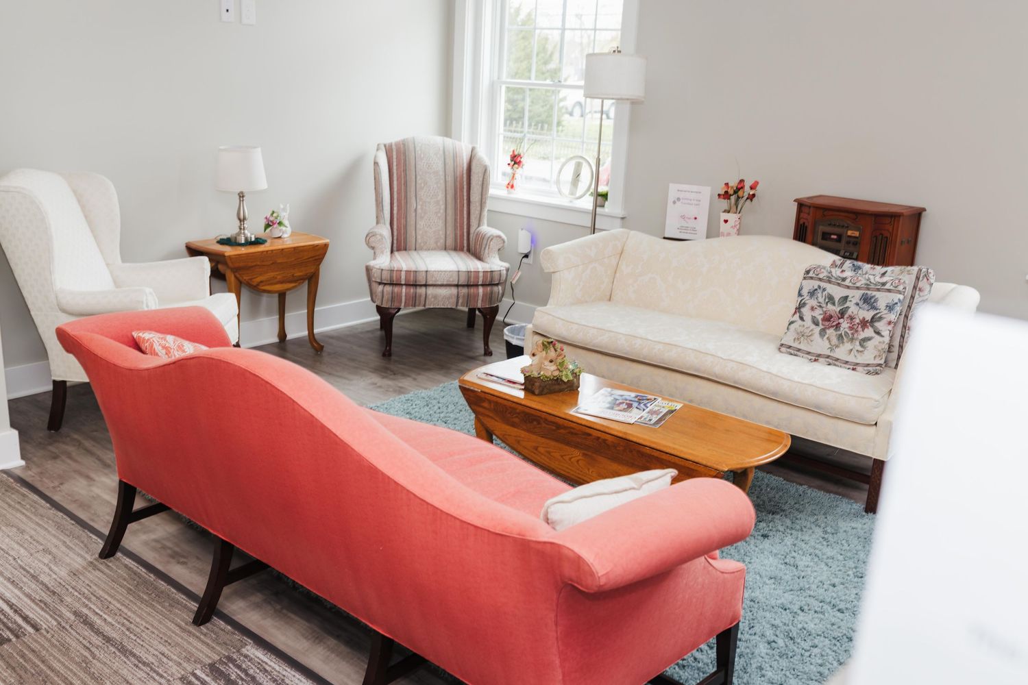 A cozy living room library space in Annville, PA with coral and beige armchairs, white sofa, wooden coffee table, and blue area rug.
