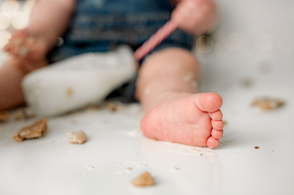 A tiny newborn baby foot rests against a light background with cookie crumbs scattered around.