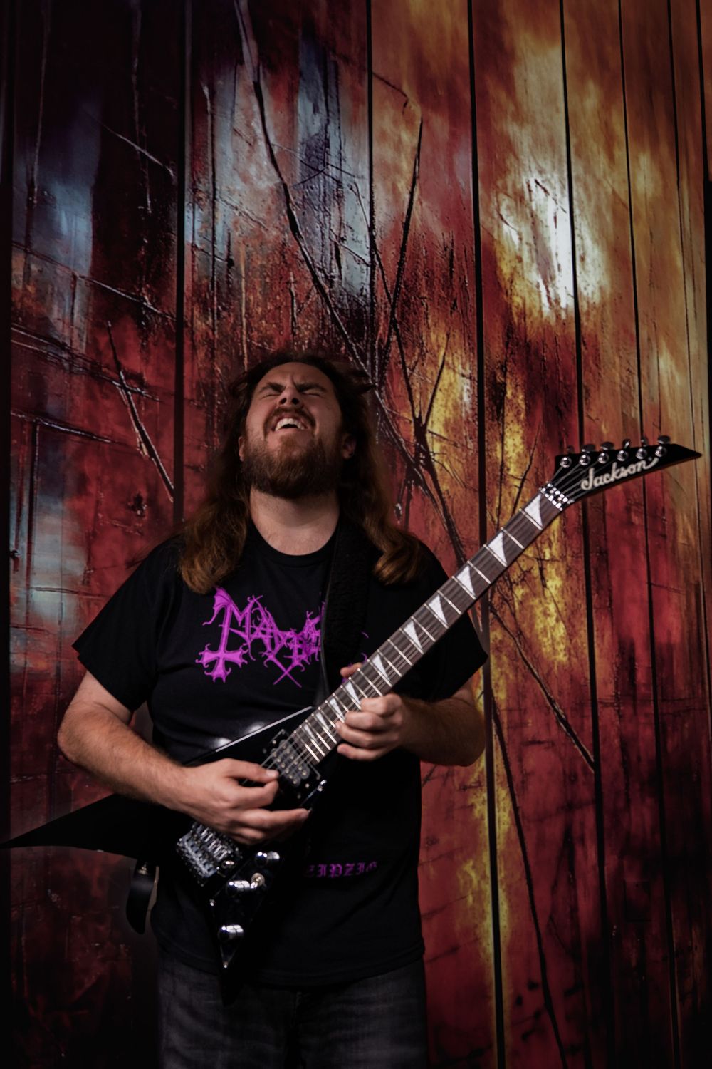 Musician in black shirt playing electric guitar against rustic red wooden wall background.